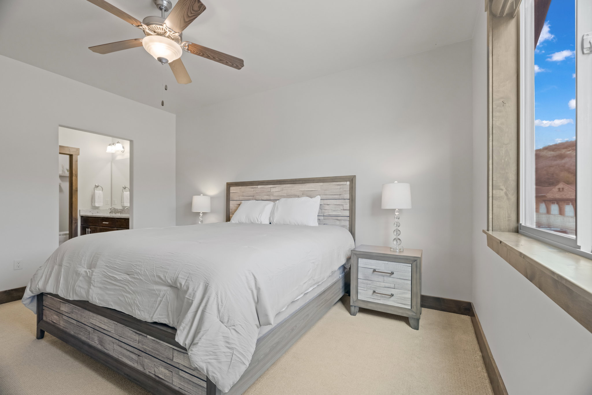 Neutral toned bedroom featuring a wood-finish ceiling fan and a window with wood trim