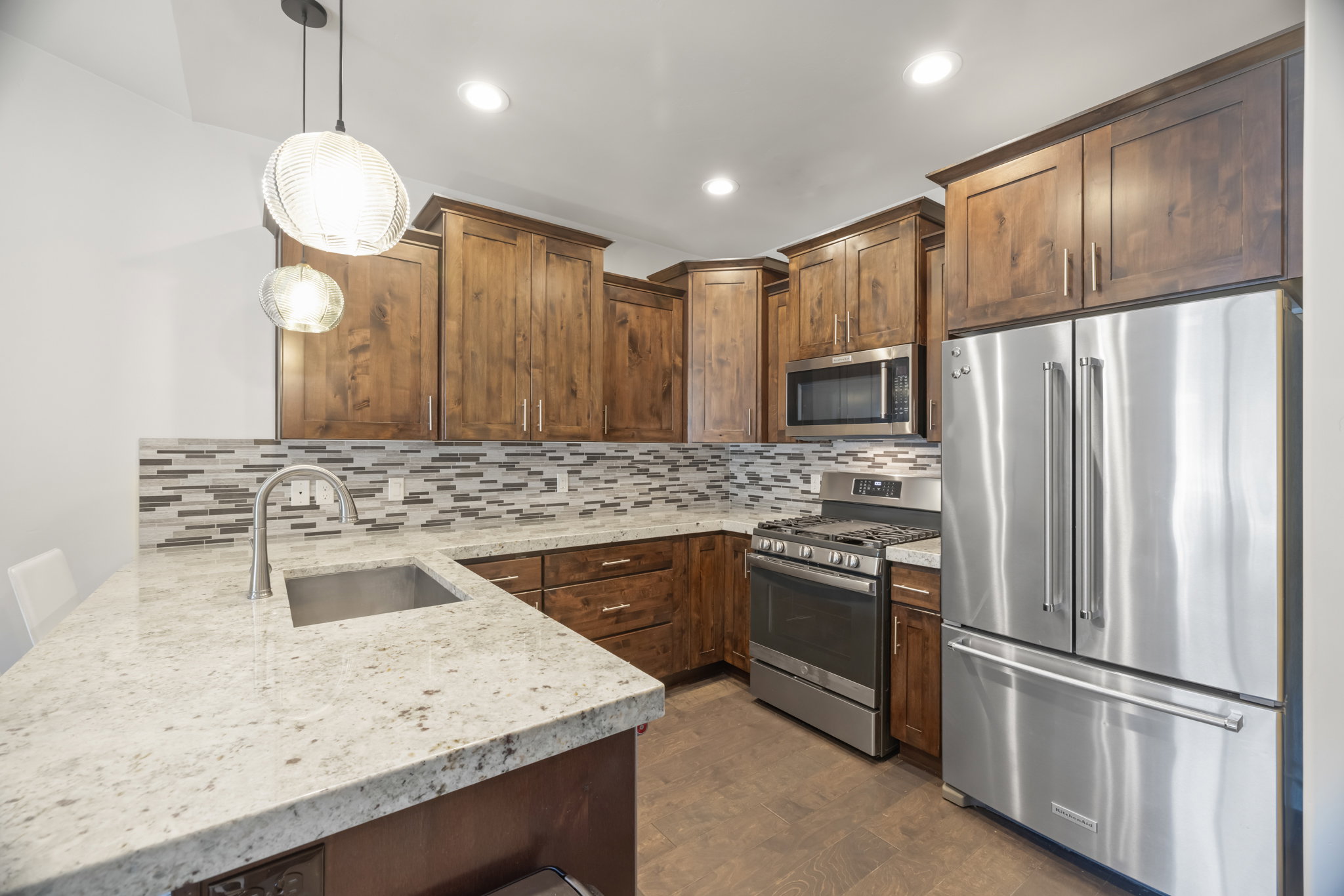 Kitchen featuring granite countertops, stainless steel appliances, wood cabinetry, mosaic tile backsplash, and recessed lighting