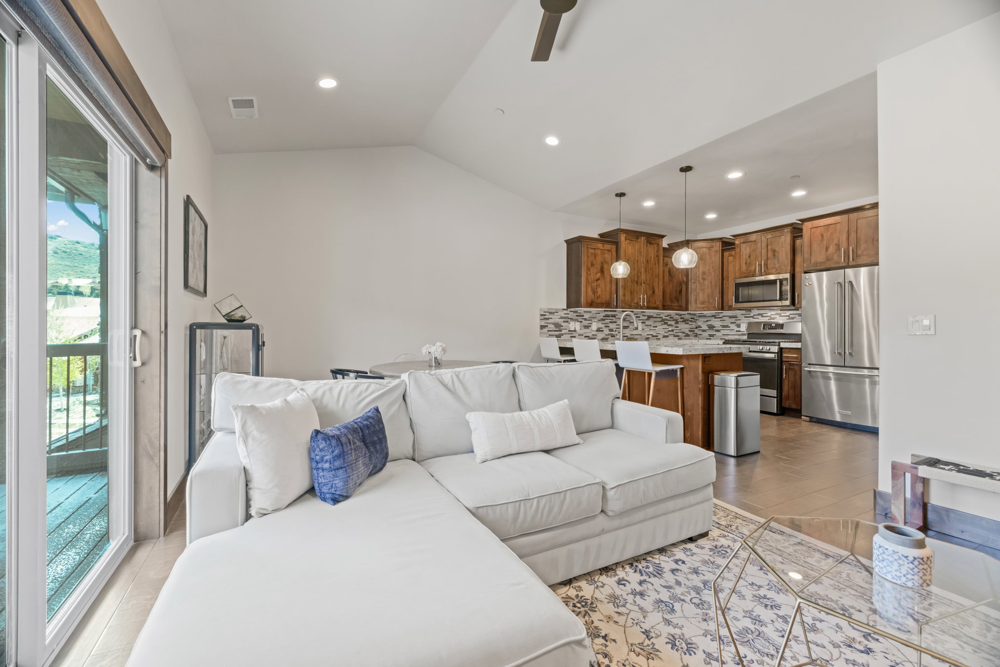 Open-concept living space featuring wood-finish cabinetry, stainless steel appliances, a multi-tone tile backsplash, recessed lighting, and a sliding glass door providing access to an outdoor area
