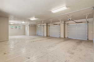 Spacious garage featuring three individual garage doors, concrete flooring, and multiple ceiling-mounted fluorescent light fixtures