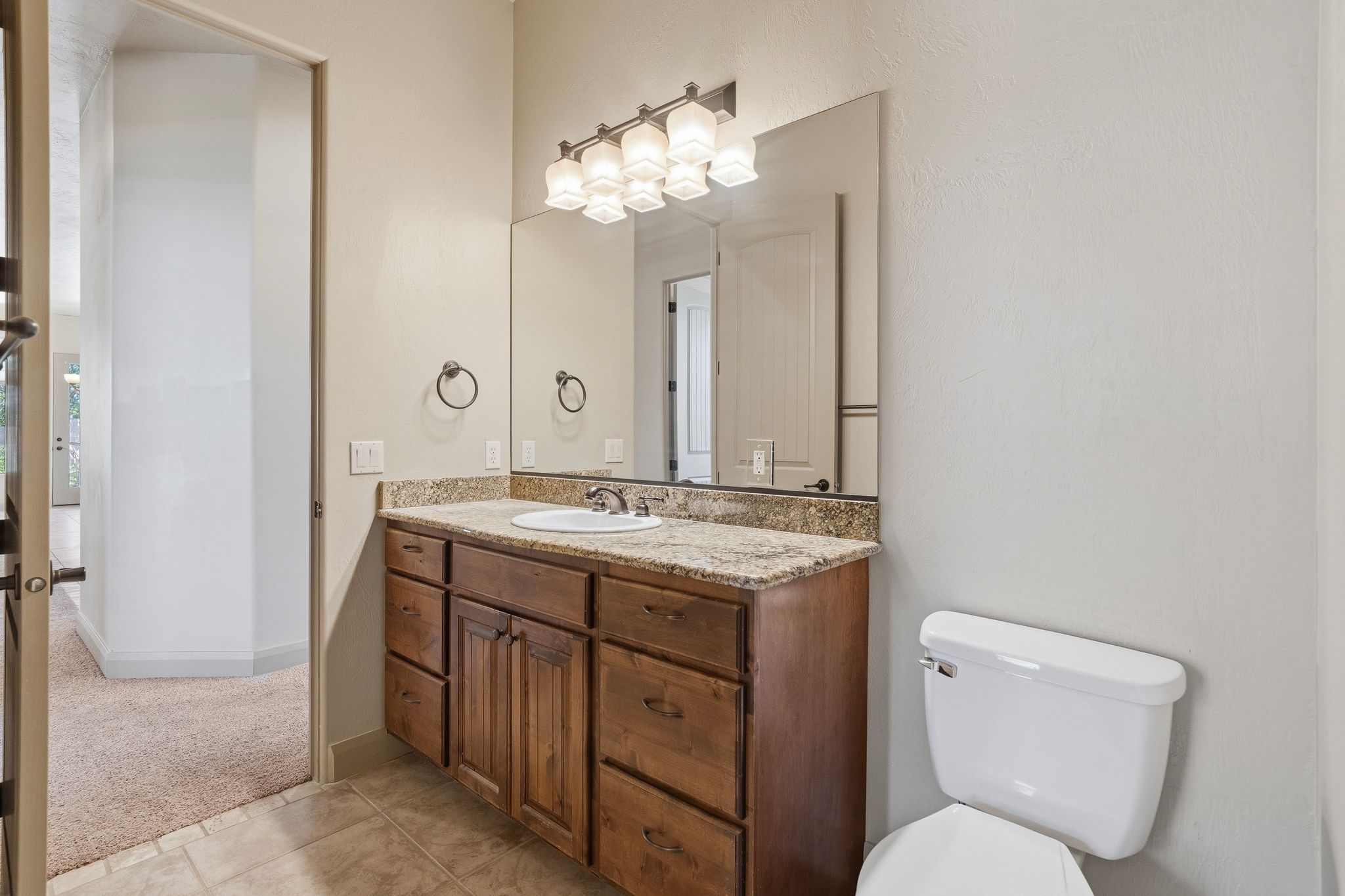 Bathroom featuring a wood-finish vanity with a granite-style countertop, undermount sink, and tiled flooring