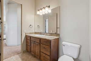 Bathroom featuring a wood-finish vanity with a granite-style countertop, undermount sink, and tiled flooring