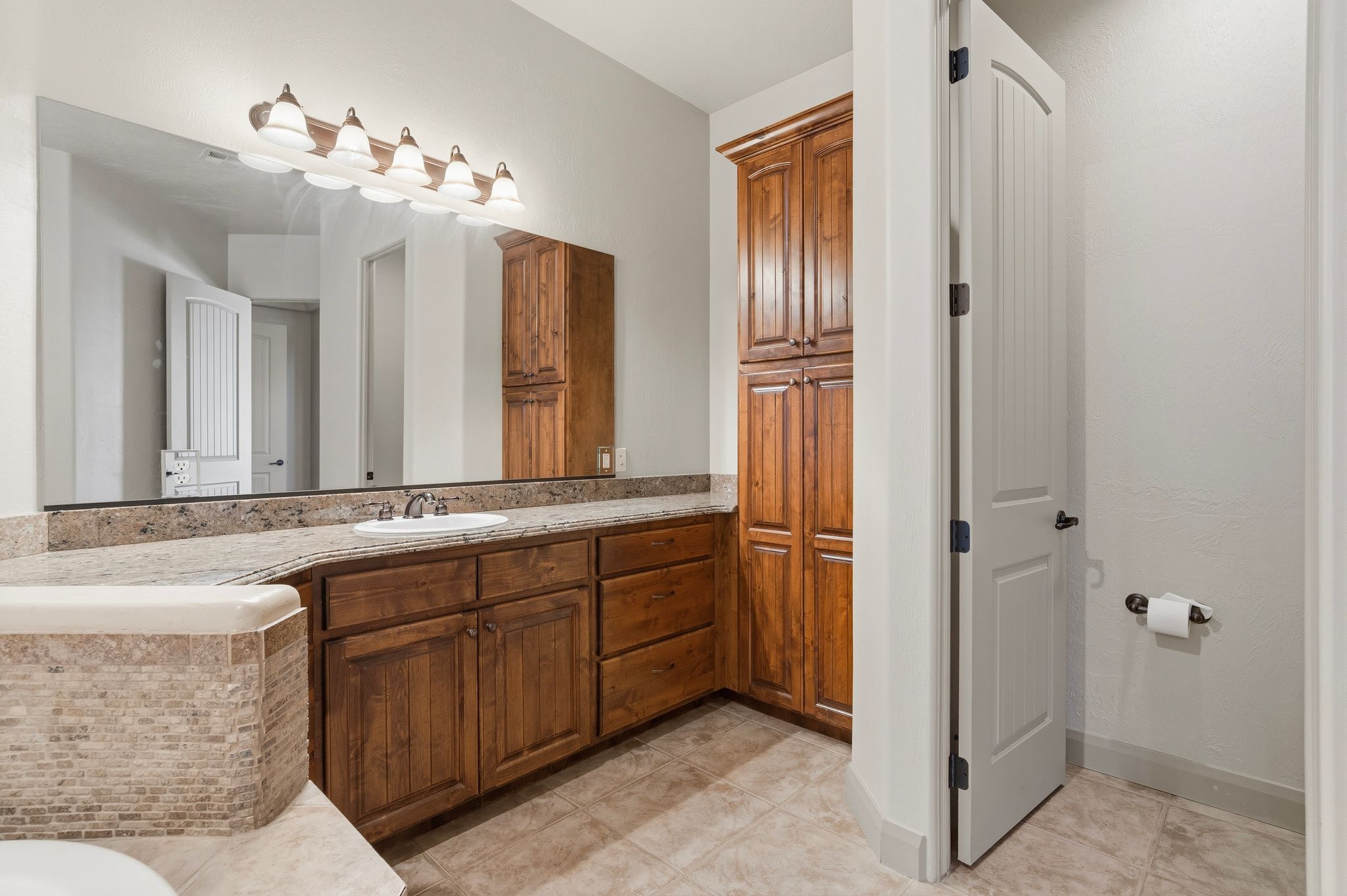 Primary suite bathroom vanity featuring a single sink, stone countertop, and wood-finish cabinetry