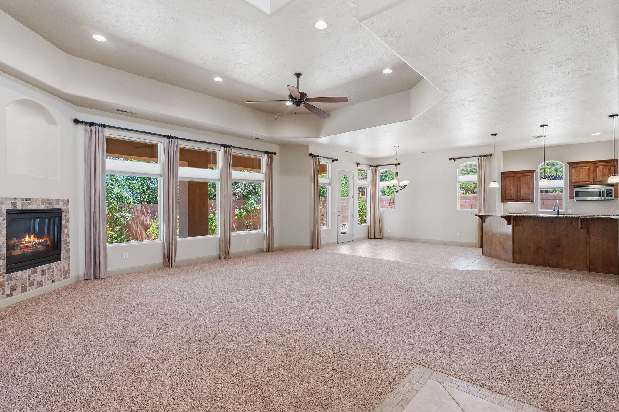 Spacious open-concept room featuring a tiled gas fireplace, multiple large windows, and a ceiling fan