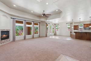 Spacious open-concept room featuring a tiled gas fireplace, multiple large windows, and a ceiling fan