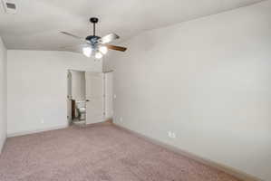 ADU spacious bedroom featuring neutral carpeting, a ceiling fan with integrated lighting, and a white paneled door revealing a bathroom with a toilet and wood-finish vanity
