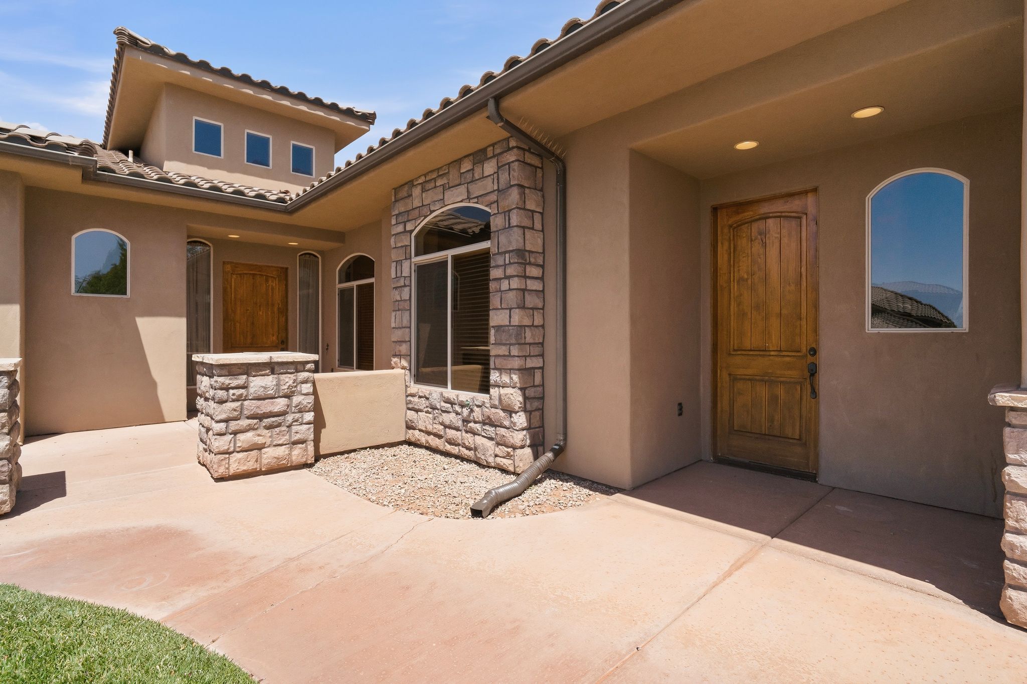 ADU exterior entry. stucco and stone exterior featuring a tile roof, arched windows, and a wood-finish entry door