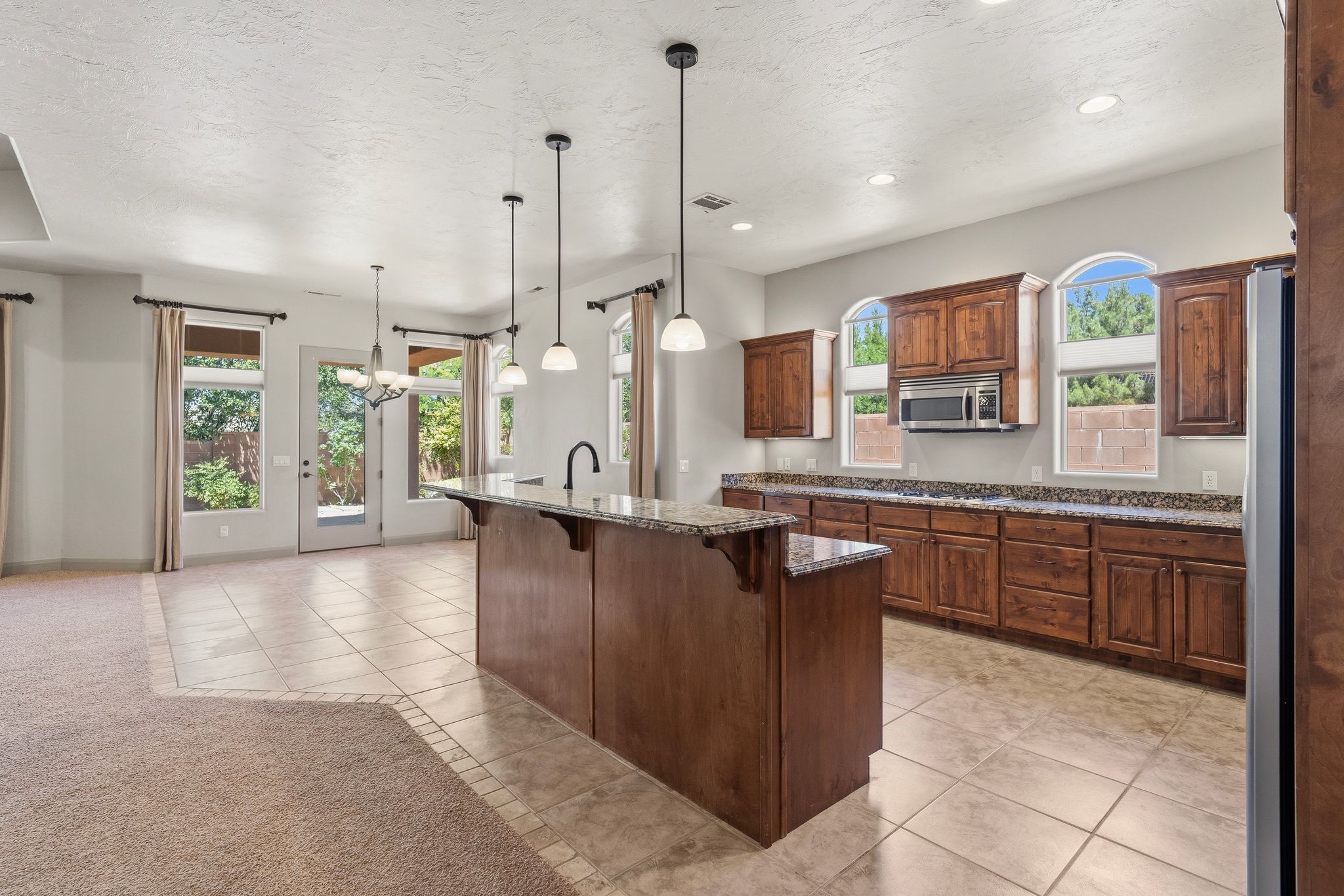 Spacious kitchen featuring rich wood cabinetry, stone countertops, and a central island with pendant lighting