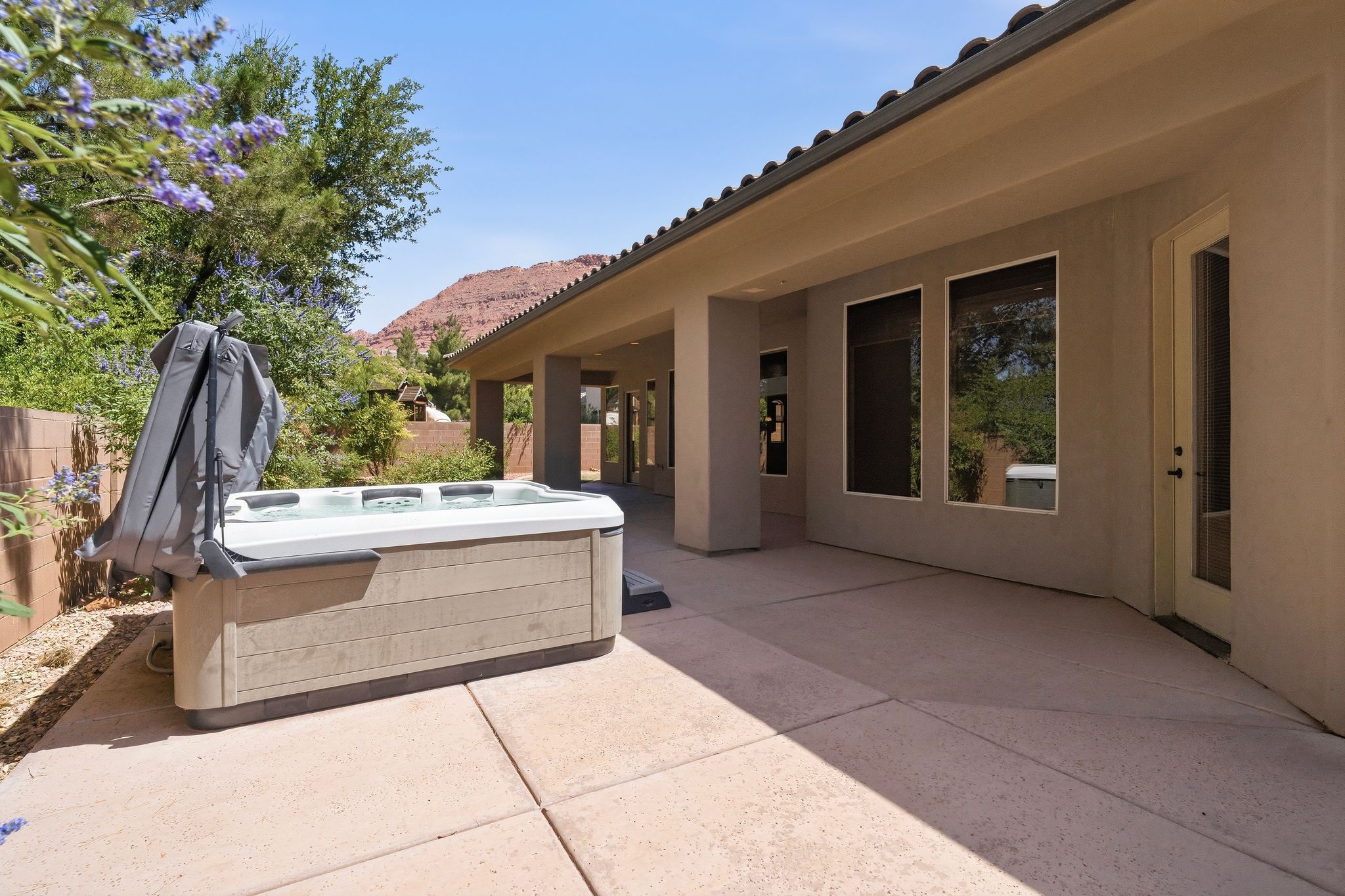 Outdoor patio featuring a built-in spa with a protective cover, a stucco exterior, and multiple windows