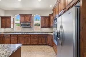 Kitchen featuring rich wood cabinetry, stainless steel appliances, speckled stone countertops, and arched windows