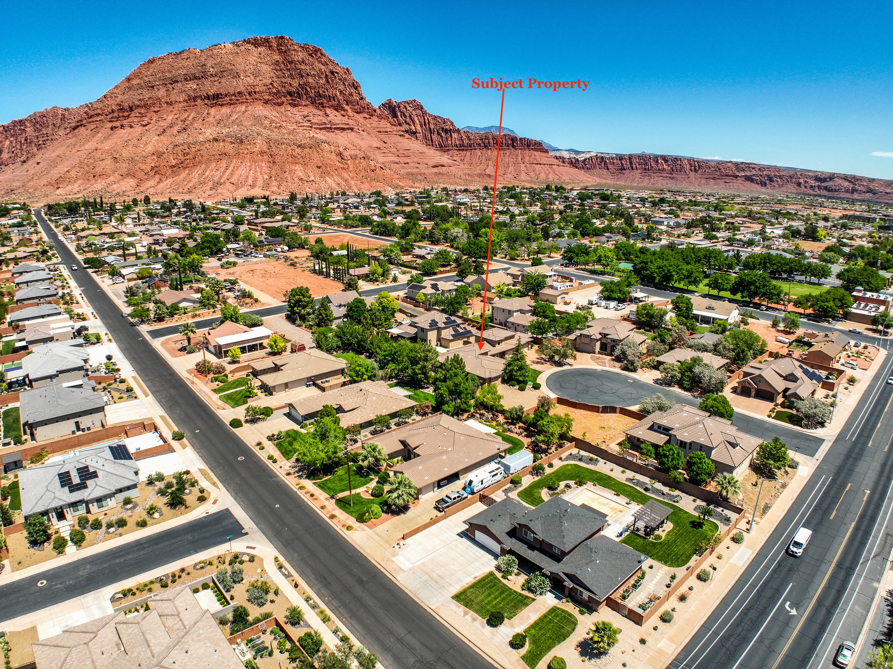 Aerial perspective showcasing the subject property within a residential neighborhood framed by distant red rock formations and a clear sky.