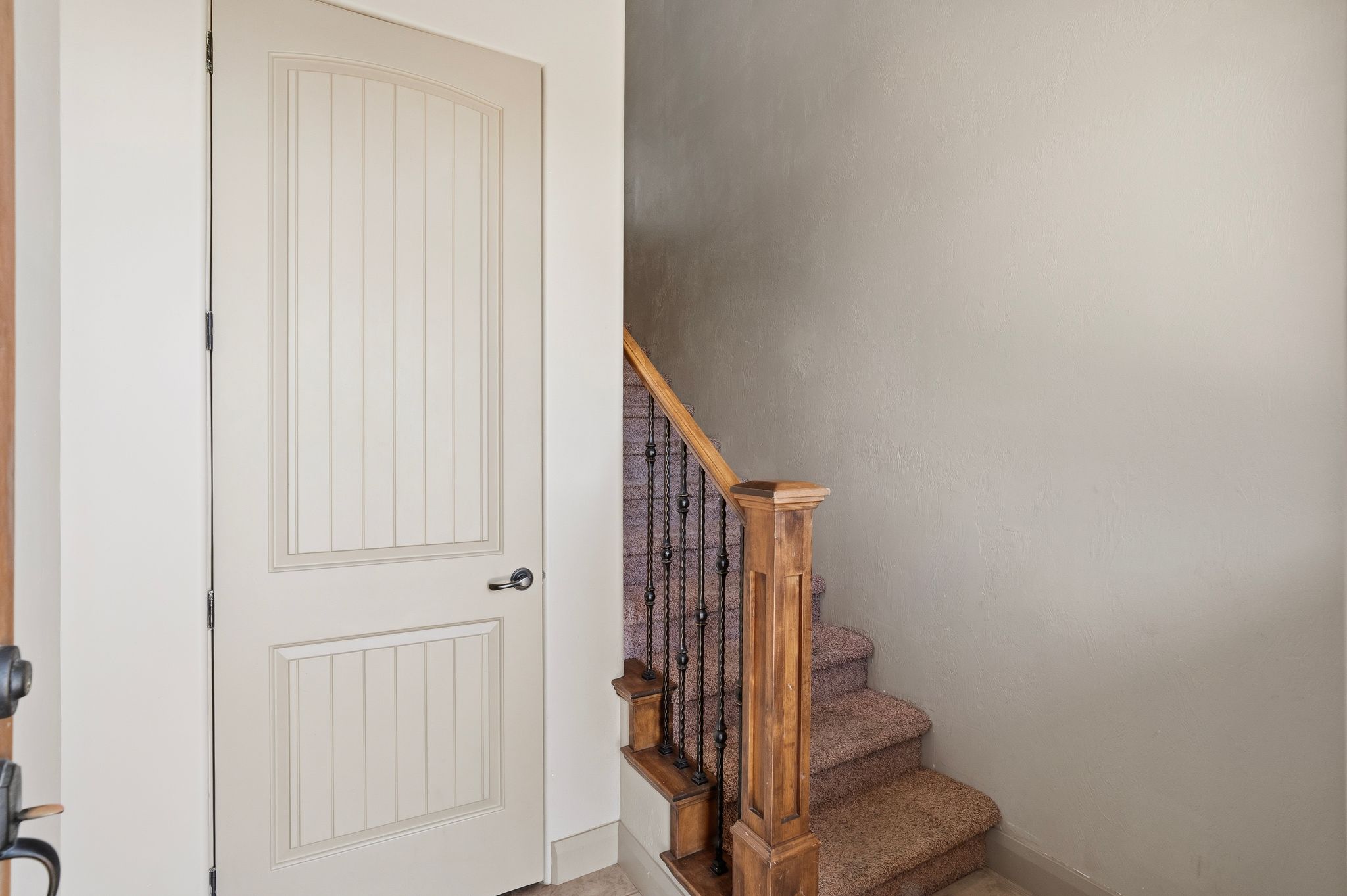 ADU entrance, arched interior door with vertical paneling and matte black hardware, complementing the carpeted staircase with wood newel post and wrought iron balusters