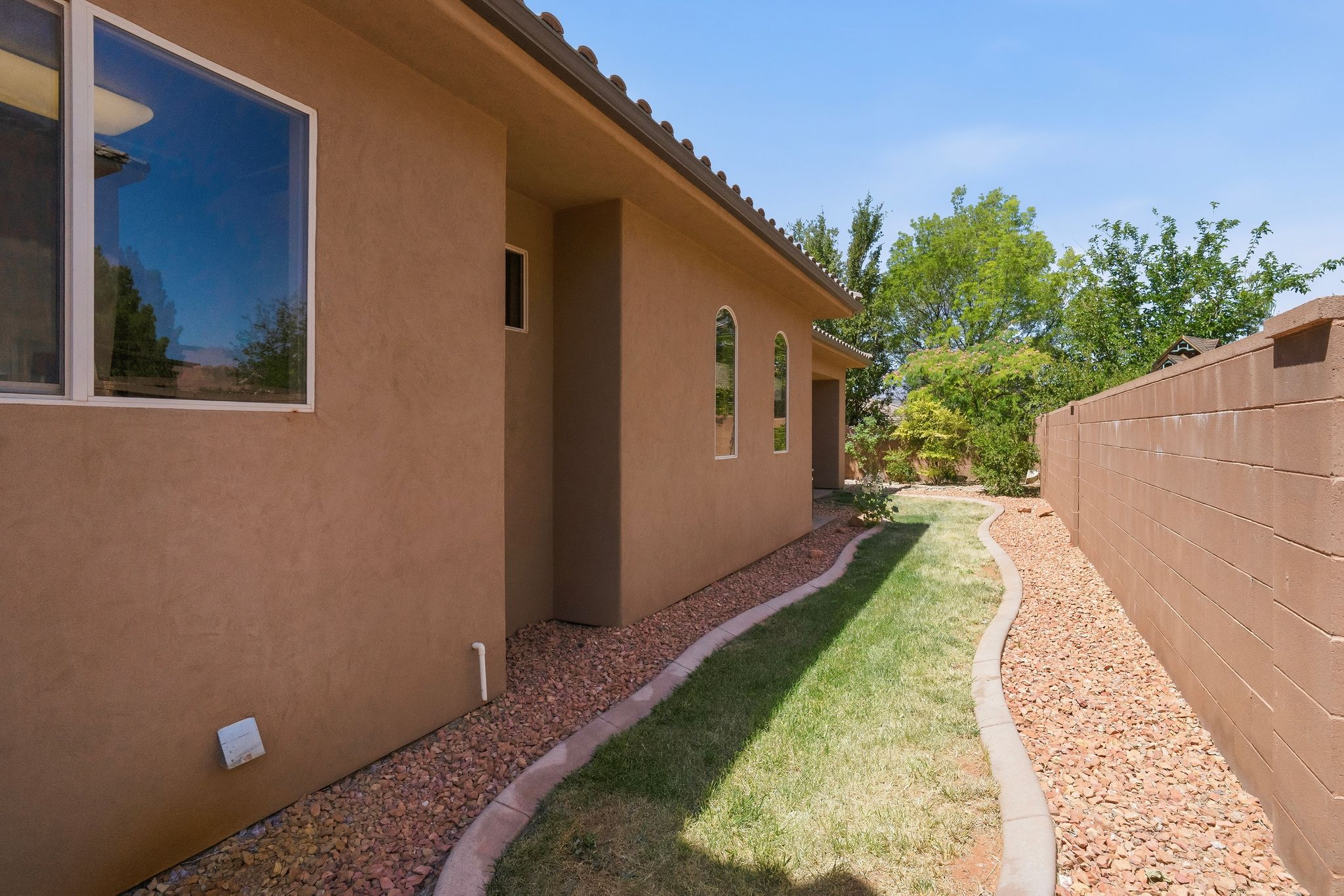 Stucco exterior with arched windows and a side yard featuring a manicured lawn, decorative rock landscaping, and a block privacy wall