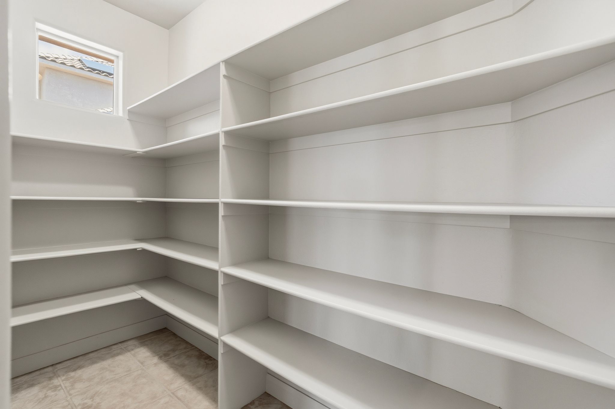 Spacious walk-in pantry featuring extensive built-in shelving, a corner window, and tile flooring