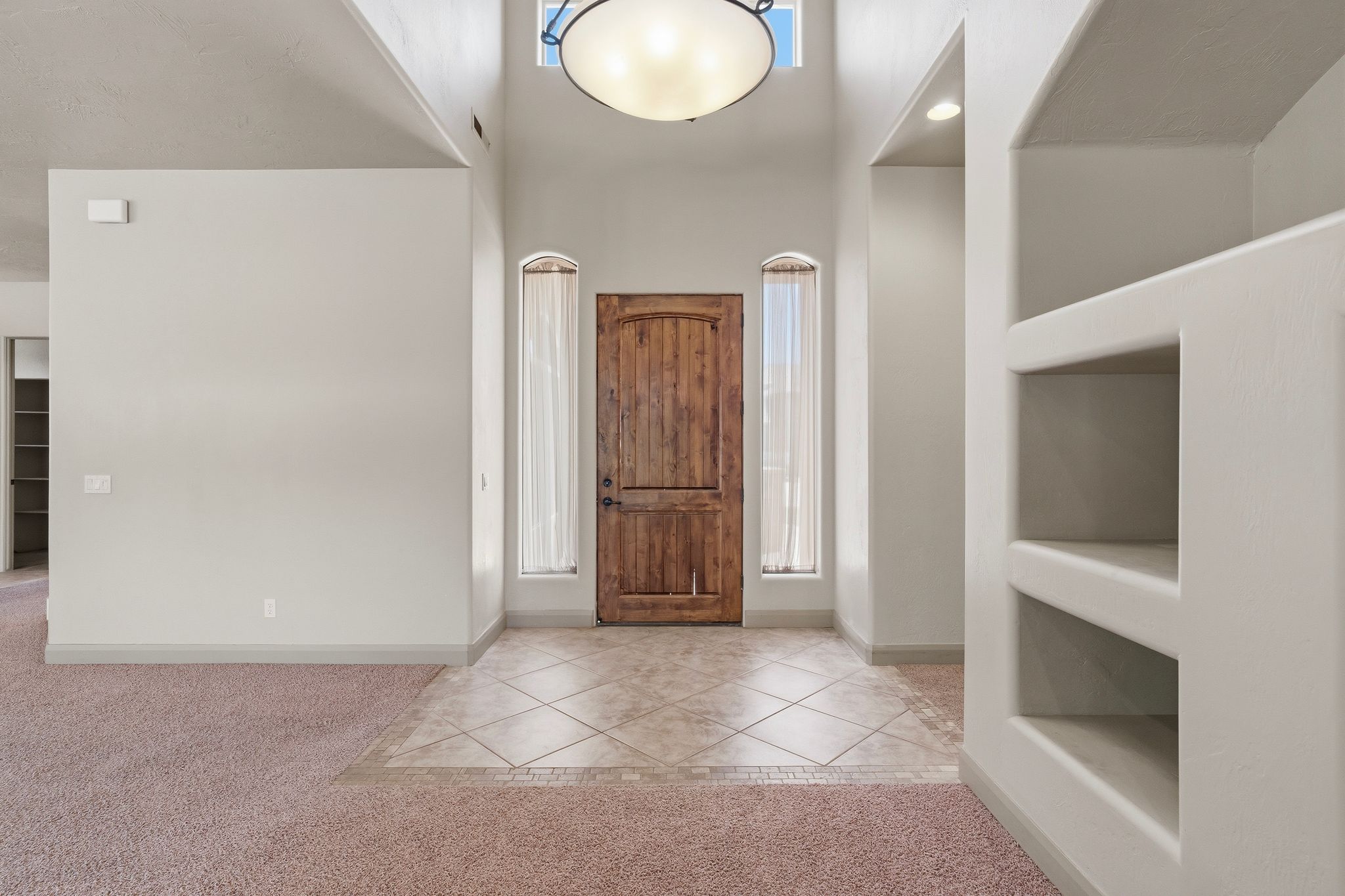 Entryway featuring a wood-panel door, arched windows with sheer drapes, tiled flooring, built-in shelving, and a vaulted ceiling with a central light fixture