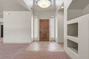 Entryway featuring a wood-panel door, arched windows with sheer drapes, tiled flooring, built-in shelving, and a vaulted ceiling with a central light fixture