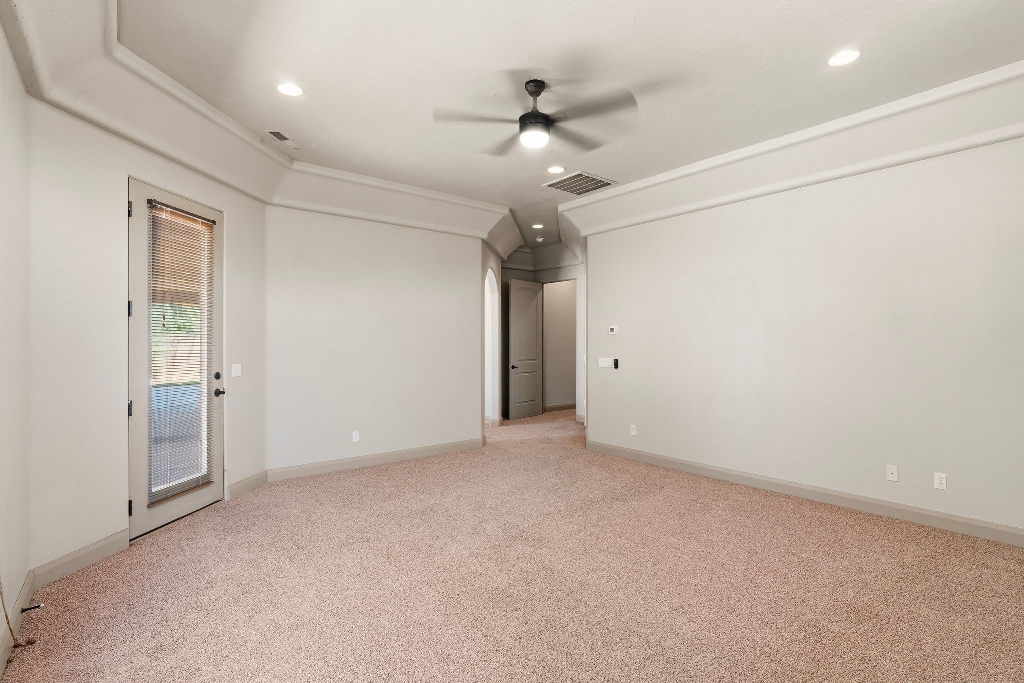 Primary suite, spacious room featuring neutral carpeting, a ceiling fan with integrated lighting, recessed ceiling lights, crown molding, and a glass-paneled exterior door
