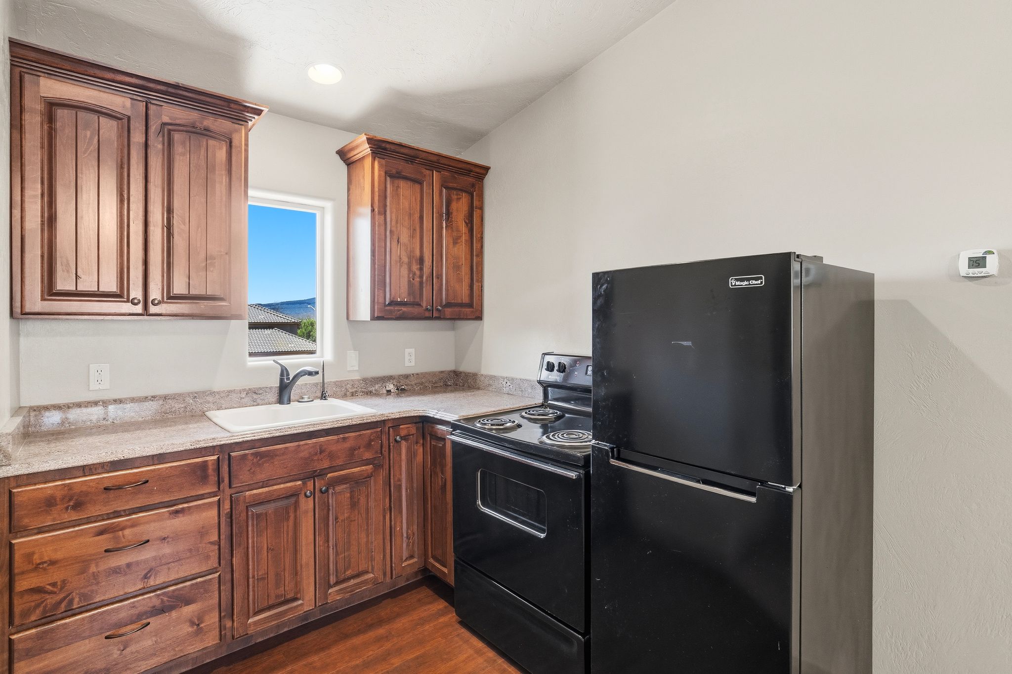 ADU kitchen featuring wood-finish cabinetry, speckled countertops, and a white sink with a black faucet