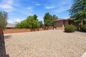 Expansive gravel side yard featuring a brick perimeter wall, mature trees, and low-maintenance landscaping