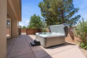 Outdoor patio featuring a hot tub, concrete paving, a block wall perimeter, mature trees, and a wrought iron gate