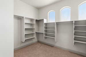 Primary suite walk-in closet featuring built-in shelving, multiple hanging rods, three arched windows, and light brown carpeting