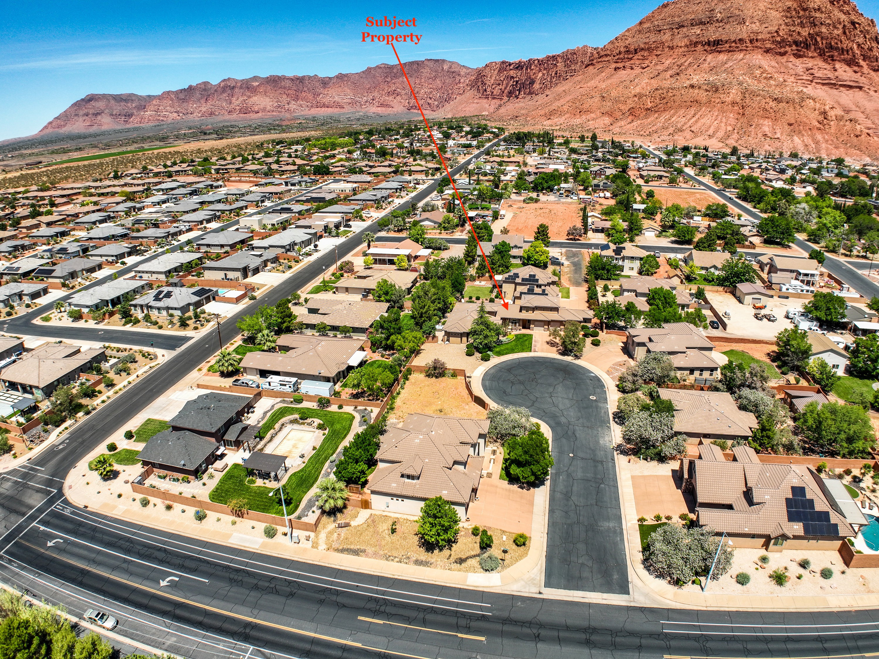 Expansive aerial perspective showcasing a residential neighborhood with a backdrop of rugged red rock formations.