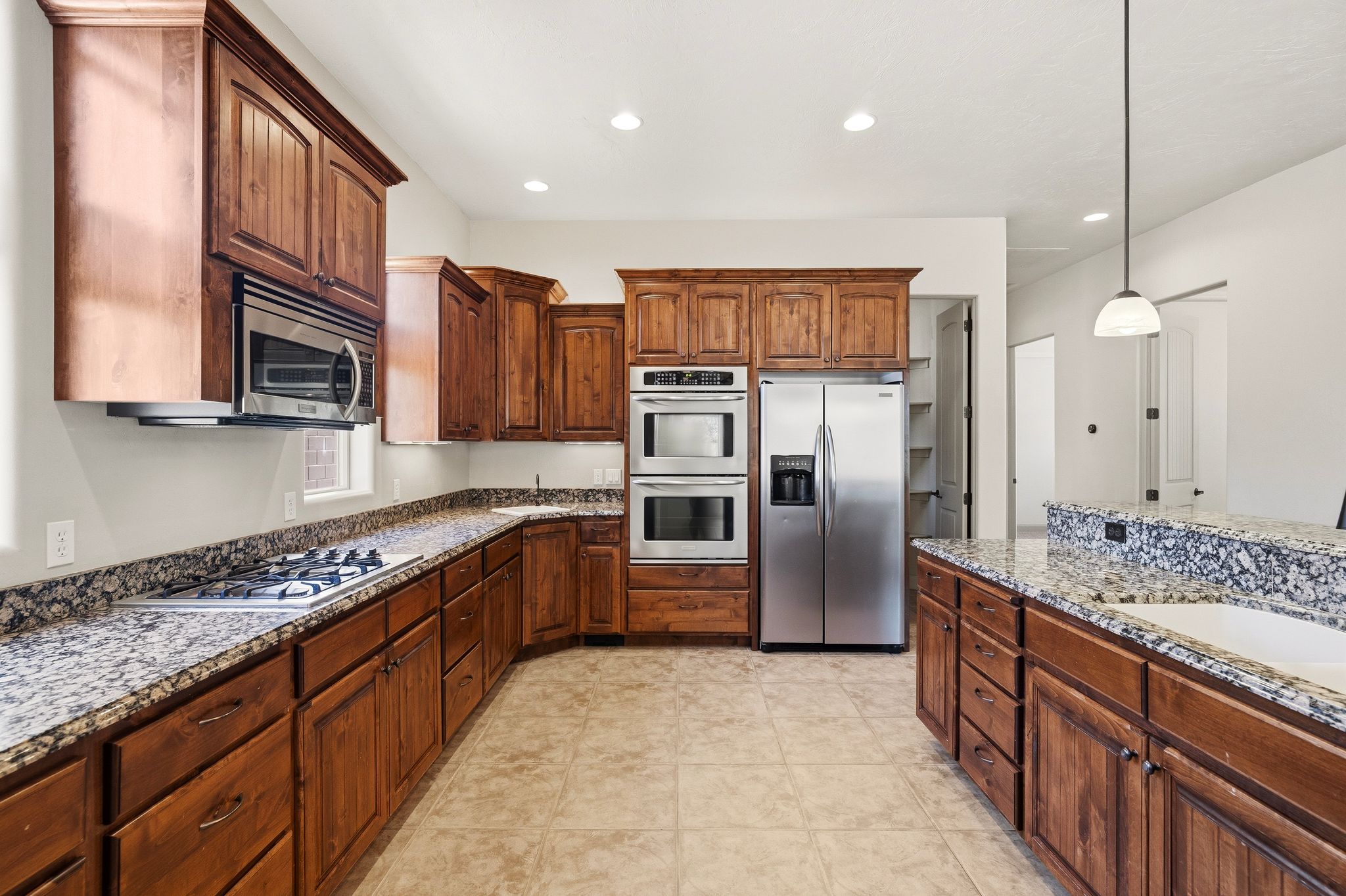 Kitchen featuring wood-finish cabinetry, granite countertops, stainless steel appliances, and tile flooring