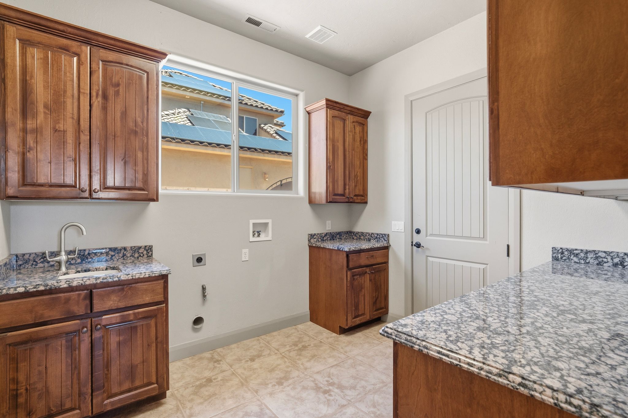 Utility room featuring wood-finish cabinetry, speckled stone countertops, and a single-basin sink with a gooseneck faucet