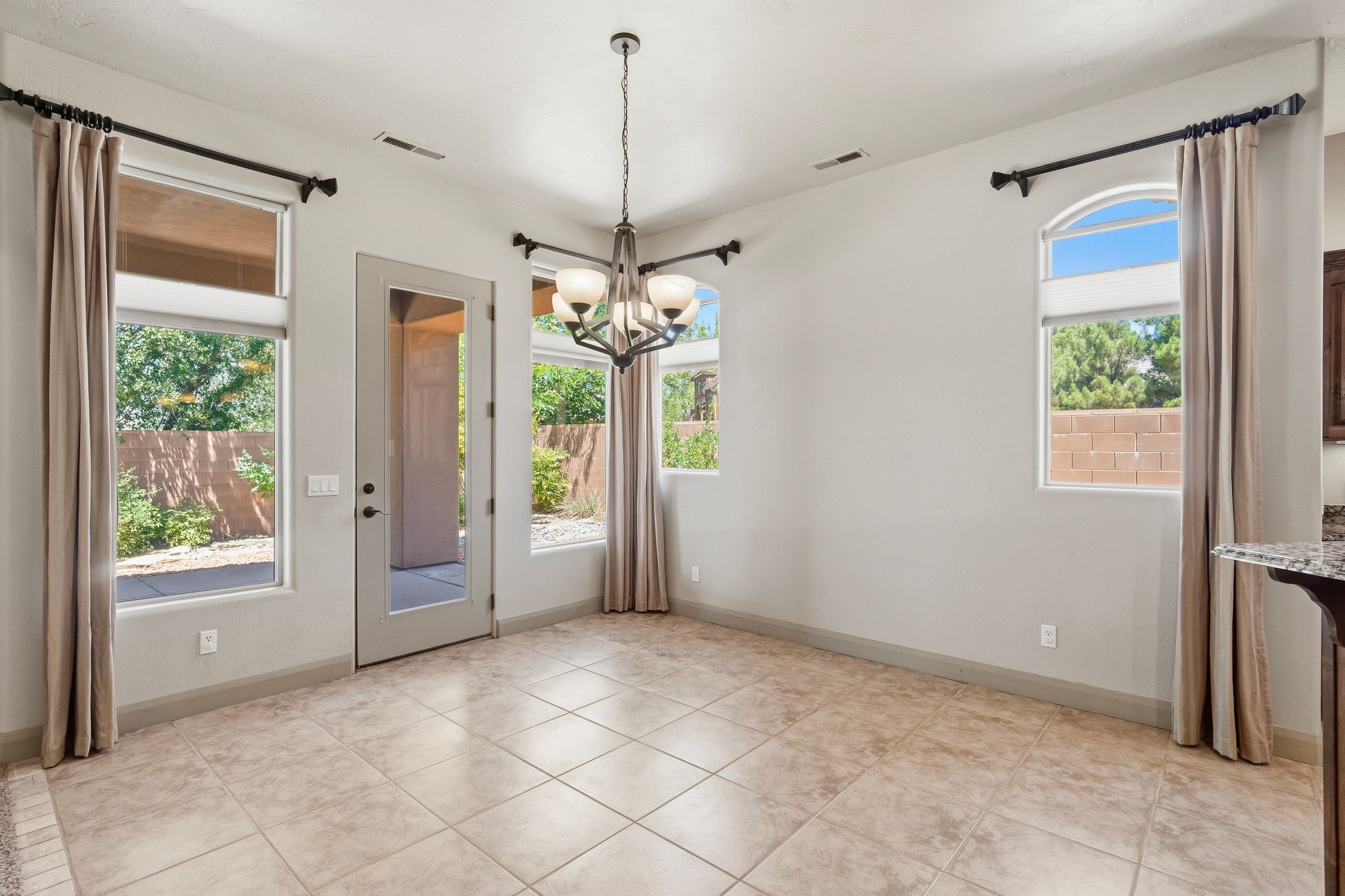 Open dining space with light-toned tile flooring, a glass-paned exterior door, multiple windows, and a chandelier with glass shades