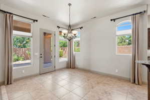 Open dining space with light-toned tile flooring, a glass-paned exterior door, multiple windows, and a chandelier with glass shades