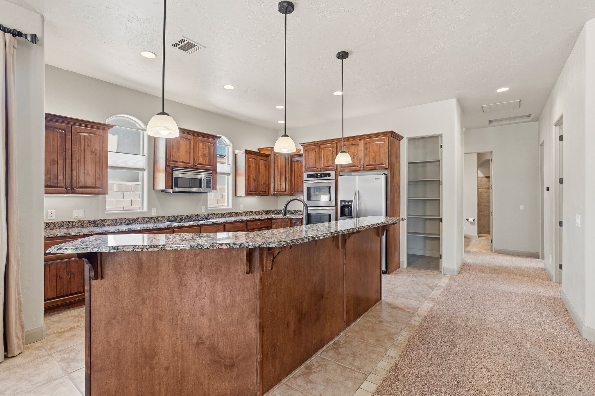 Kitchen featuring wood cabinetry, stainless steel appliances, granite countertops, and an island with pendant lighting