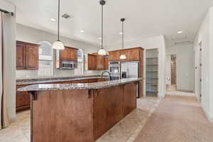 Kitchen featuring wood cabinetry, stainless steel appliances, granite countertops, and an island with pendant lighting