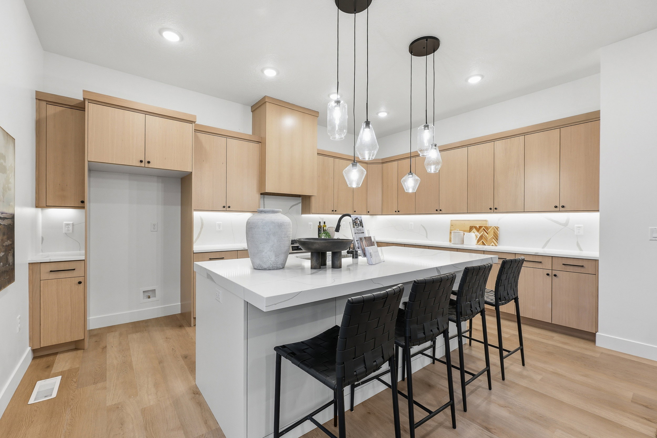 Contemporary kitchen featuring light wood-finish cabinetry, a large center island with seating, pendant lighting, under-cabinet lighting, and light-toned countertops with a matching backsplash