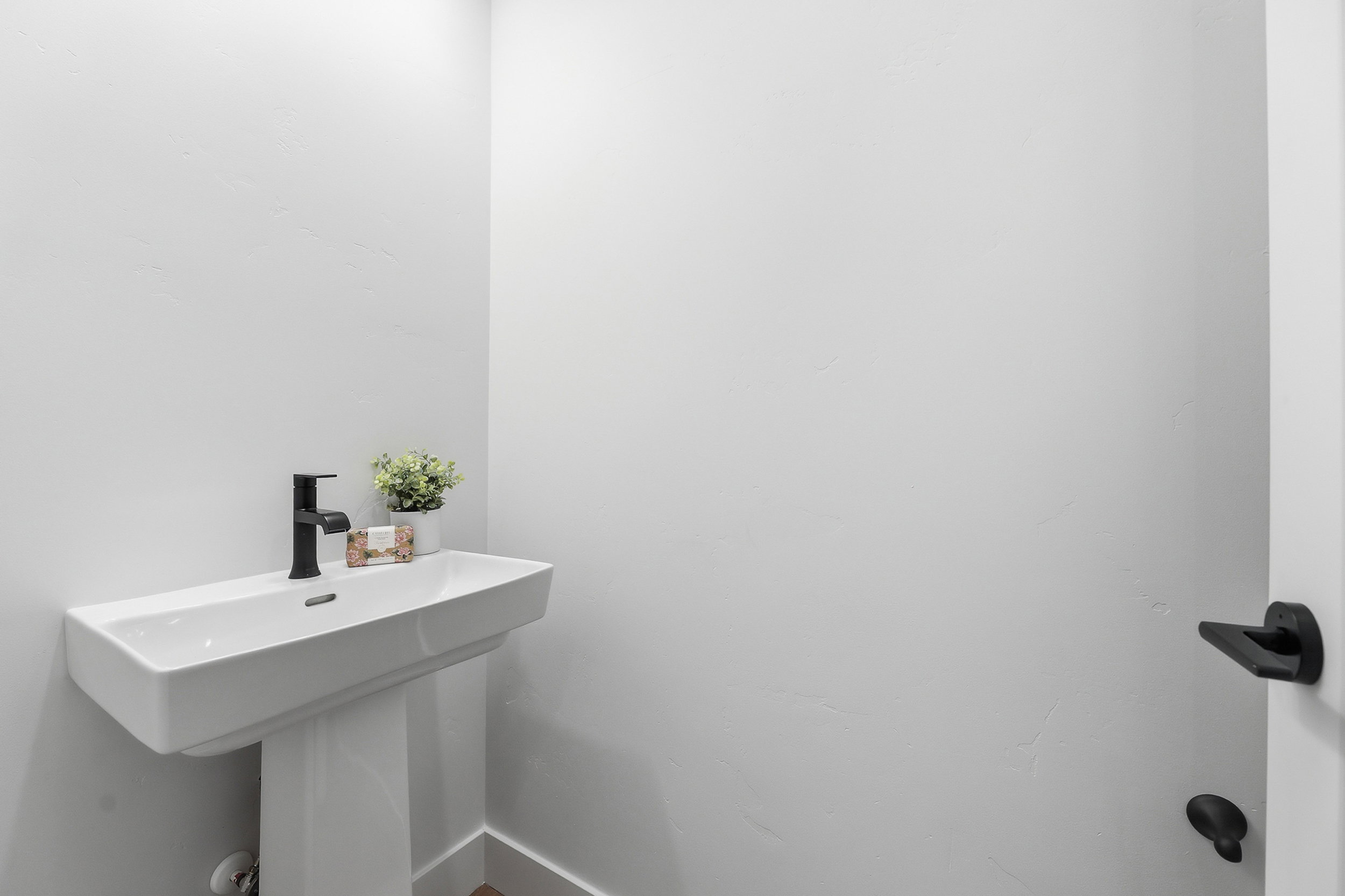 Pedestal sink with a rectangular basin, matte black wall-mounted faucet, and light-toned walls