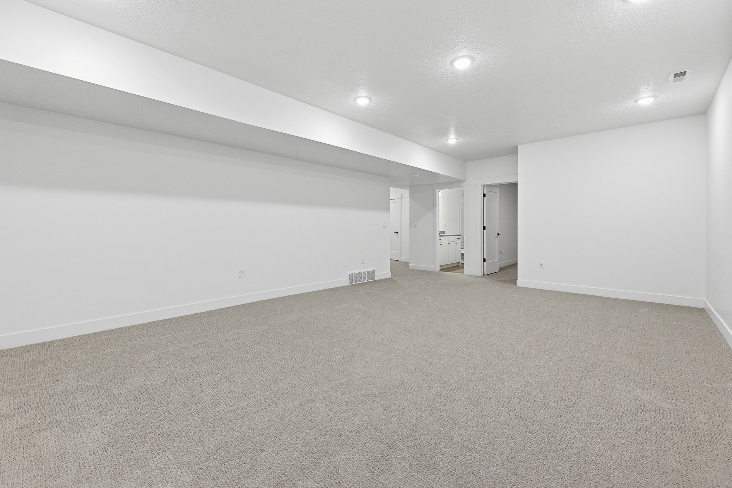 Spacious room featuring light-toned carpeting, white walls, and recessed lighting