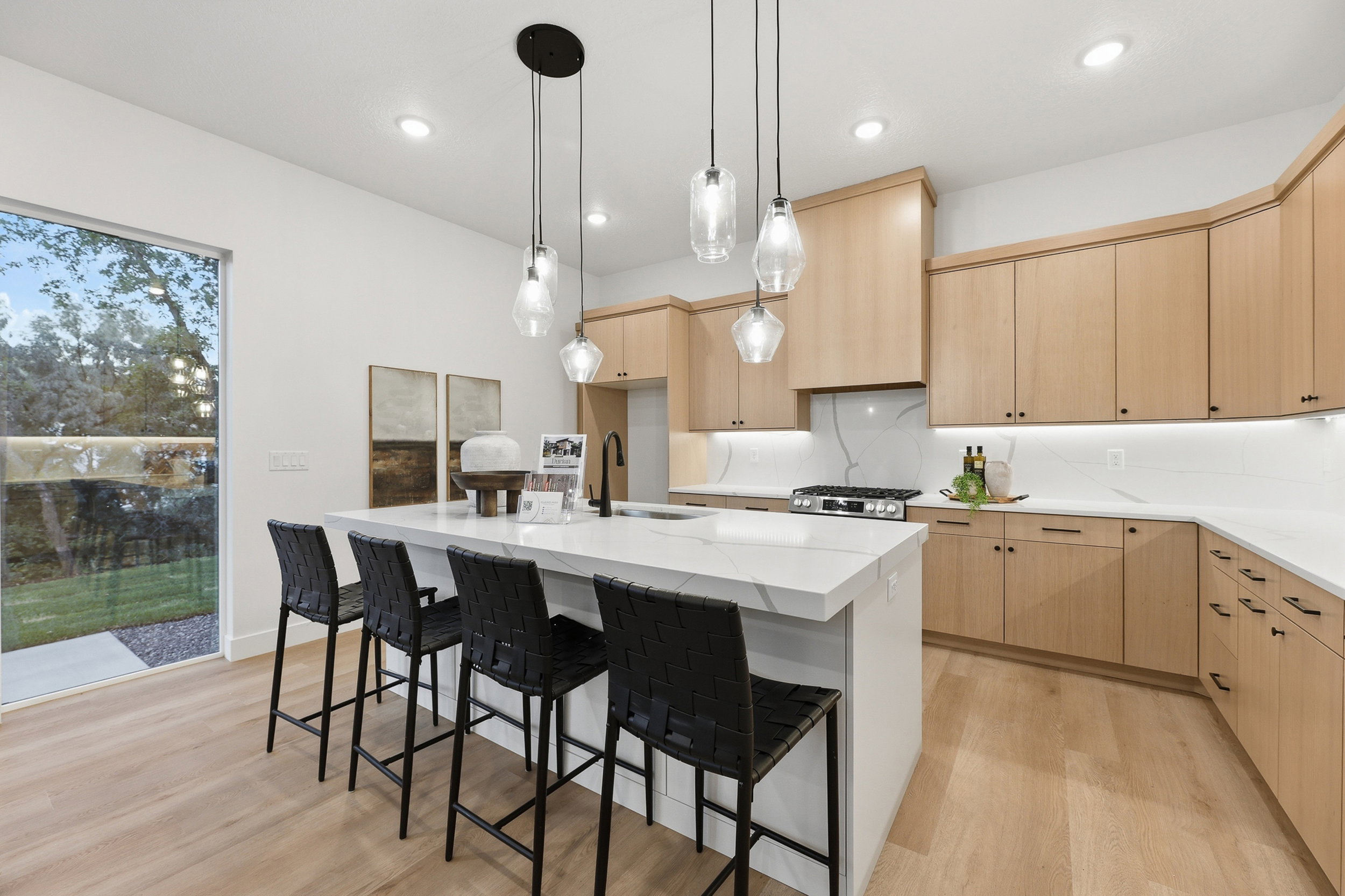 Modern kitchen featuring a waterfall island with pendant lighting, light wood-finish cabinetry, white countertops, a gas range, and wood-finish flooring