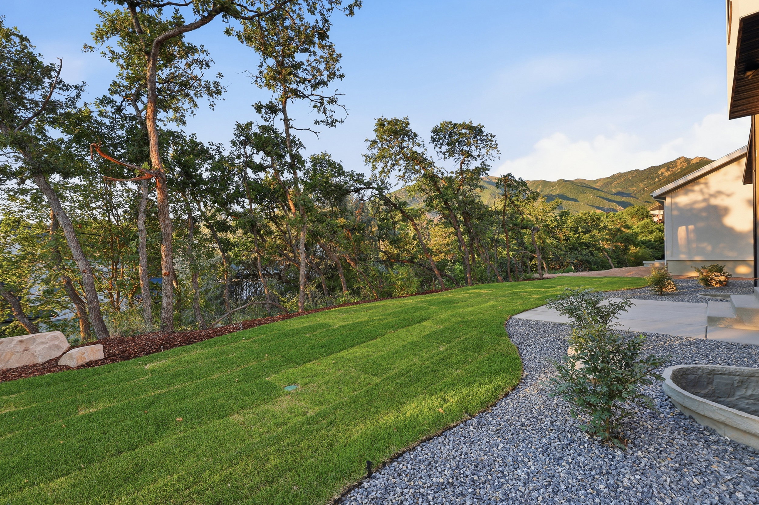 Expansive lawn with a gentle slope, bordered by mature trees and a gravel pathway