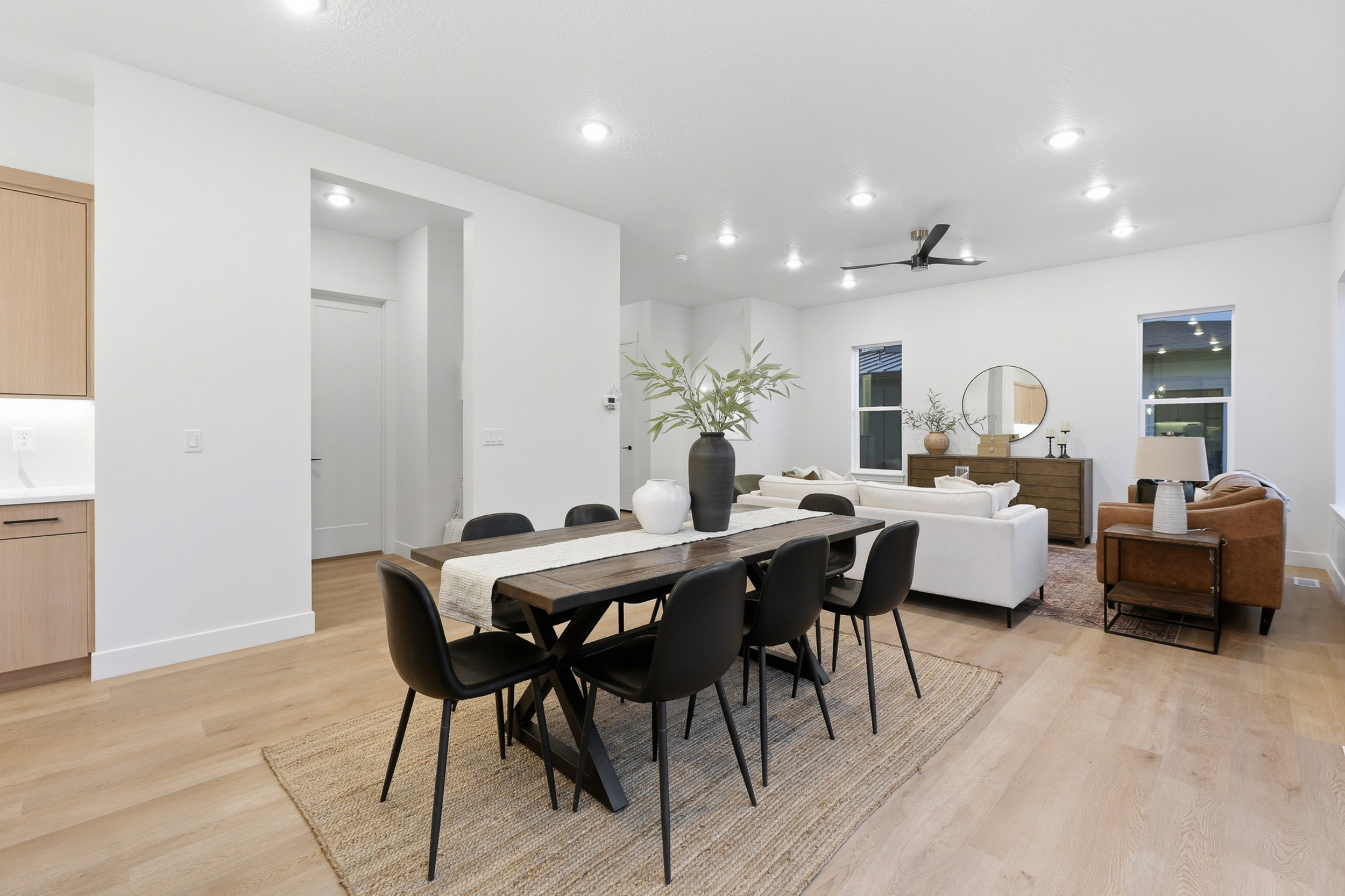 Open-concept living space featuring wood-finish flooring, recessed lighting, and a dark-toned dining table with seating