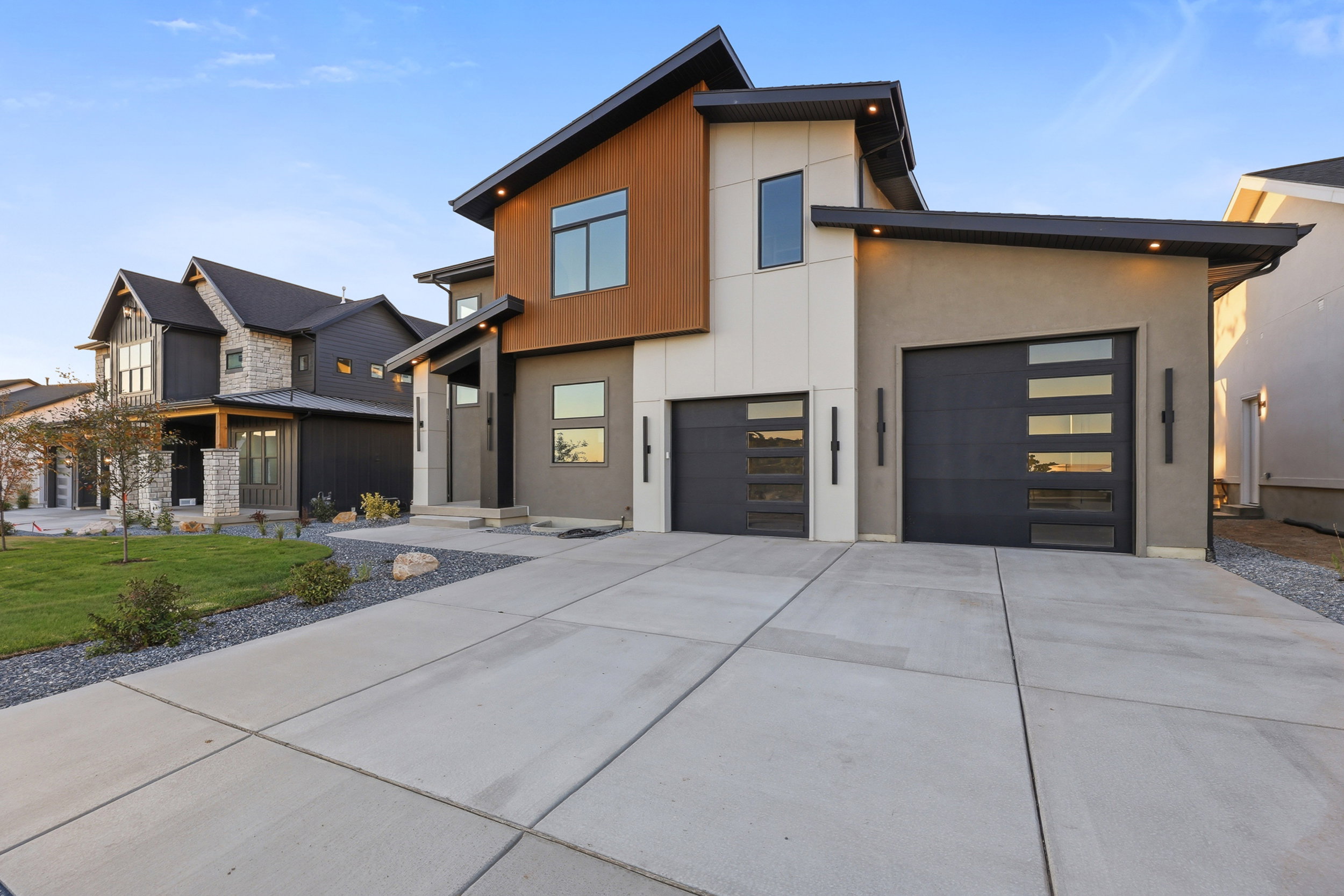 Modern architectural exterior featuring multiple material finishes, a dark trim roofline, and dual garage doors with frosted window inserts