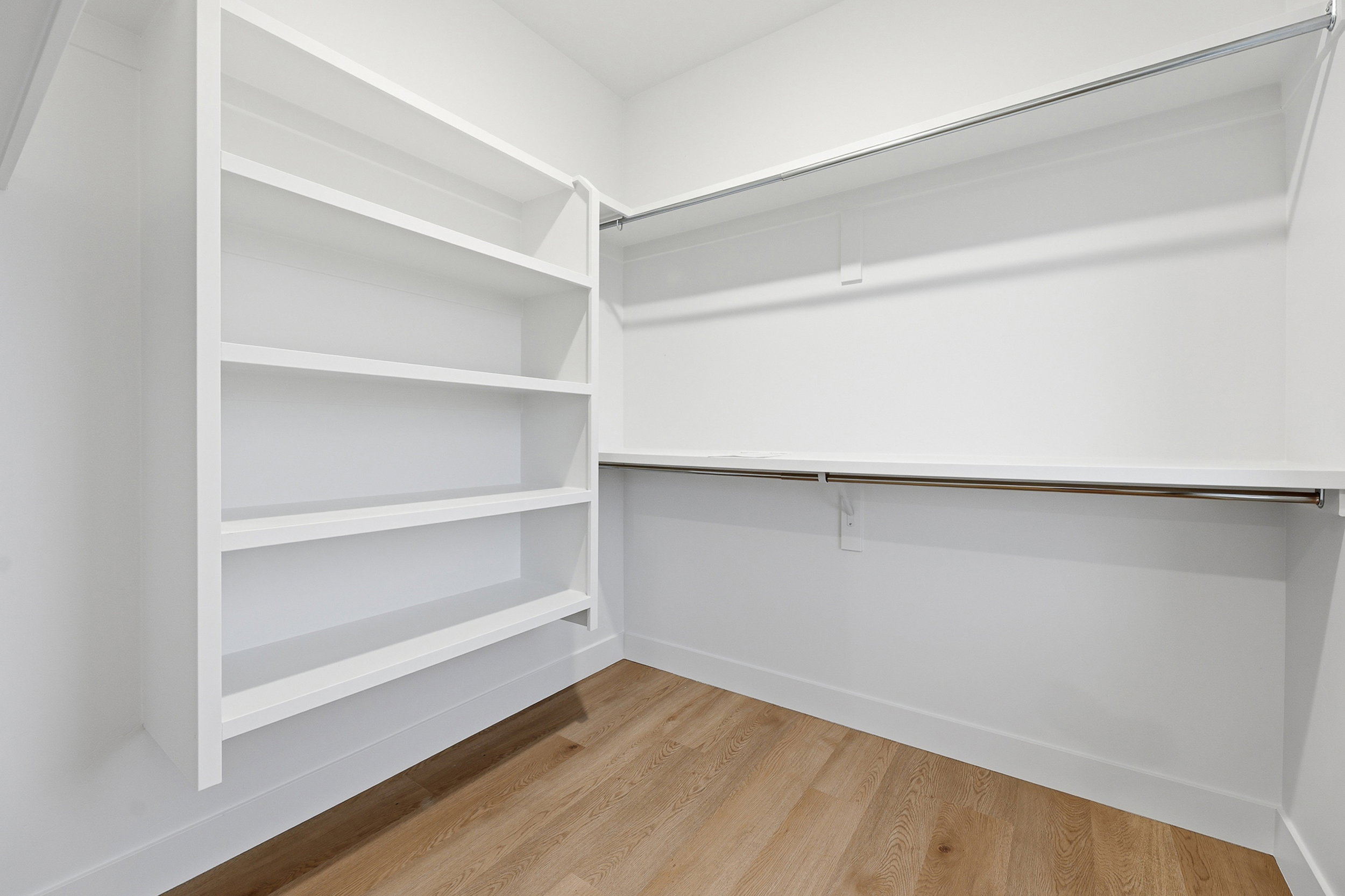 Walk-in closet featuring built-in shelving, two hanging rods, upper storage shelf, white trim, and wood-finish flooring