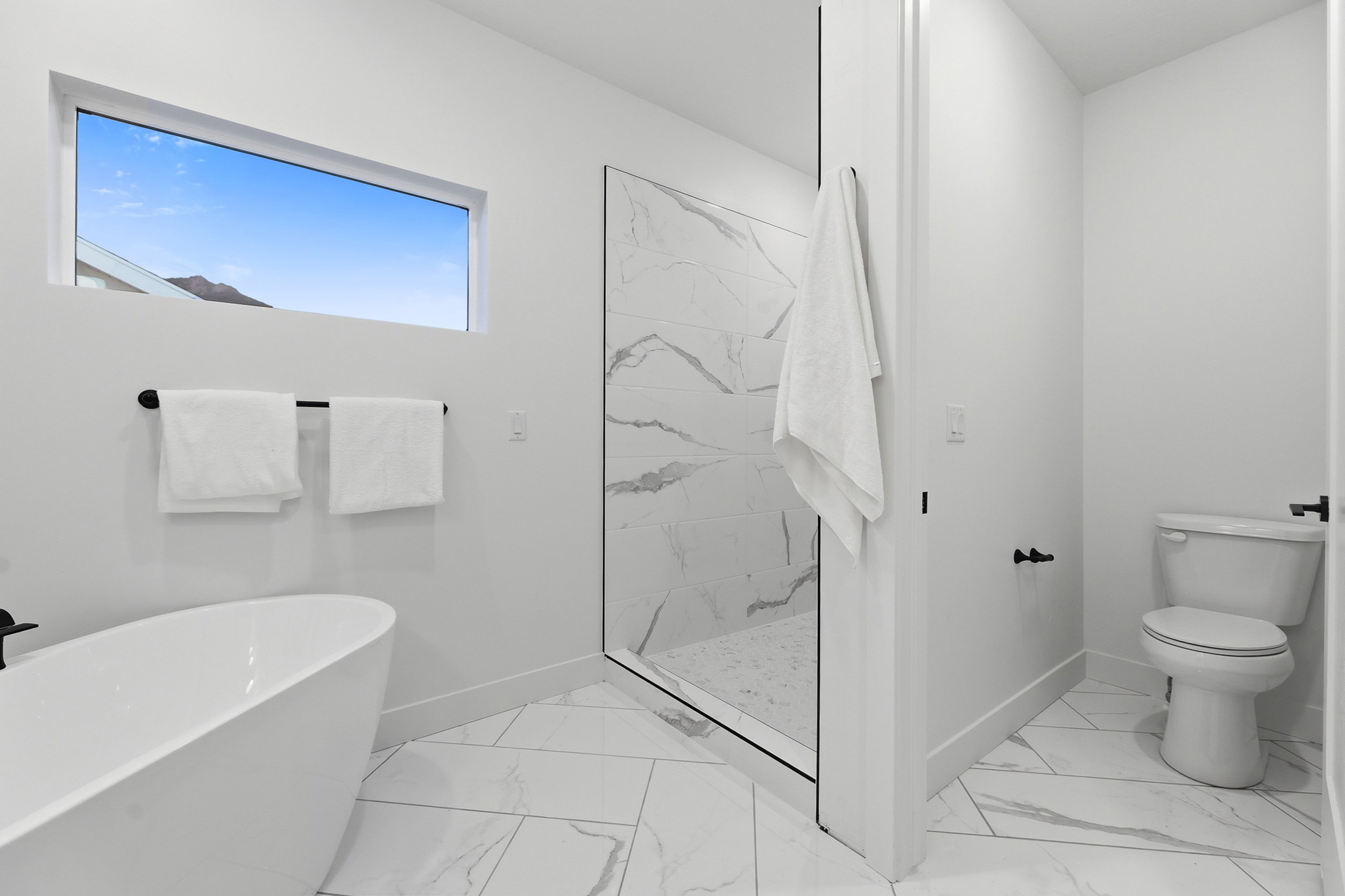 Freestanding soaking tub complemented by a spacious glass-enclosed shower with large format marble-look tile