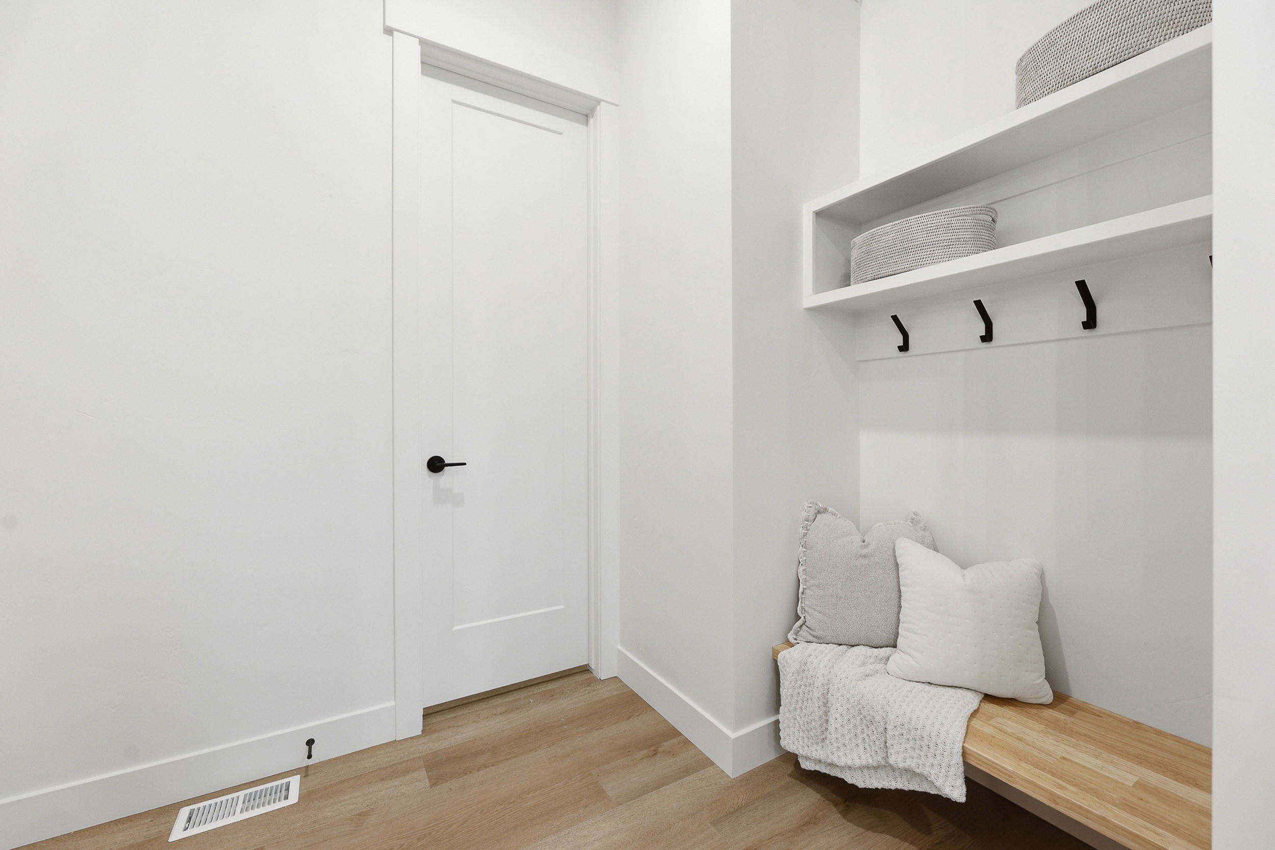 Built-in mudroom bench featuring wood-finish seating, white shelving, and black coat hooks