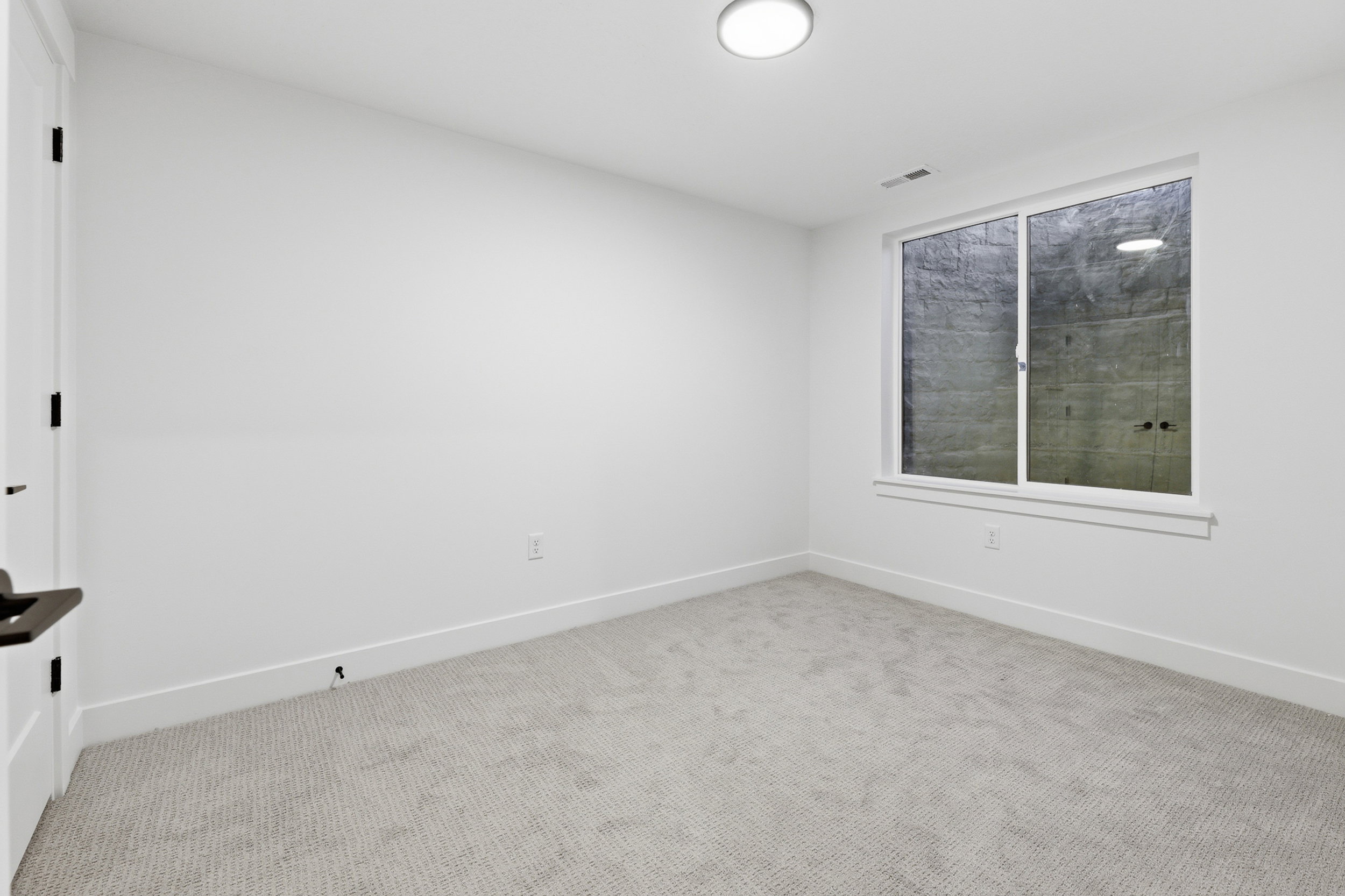 Bright interior room featuring a large window, light-colored carpeting, white walls, and a contemporary flush-mount ceiling light fixture