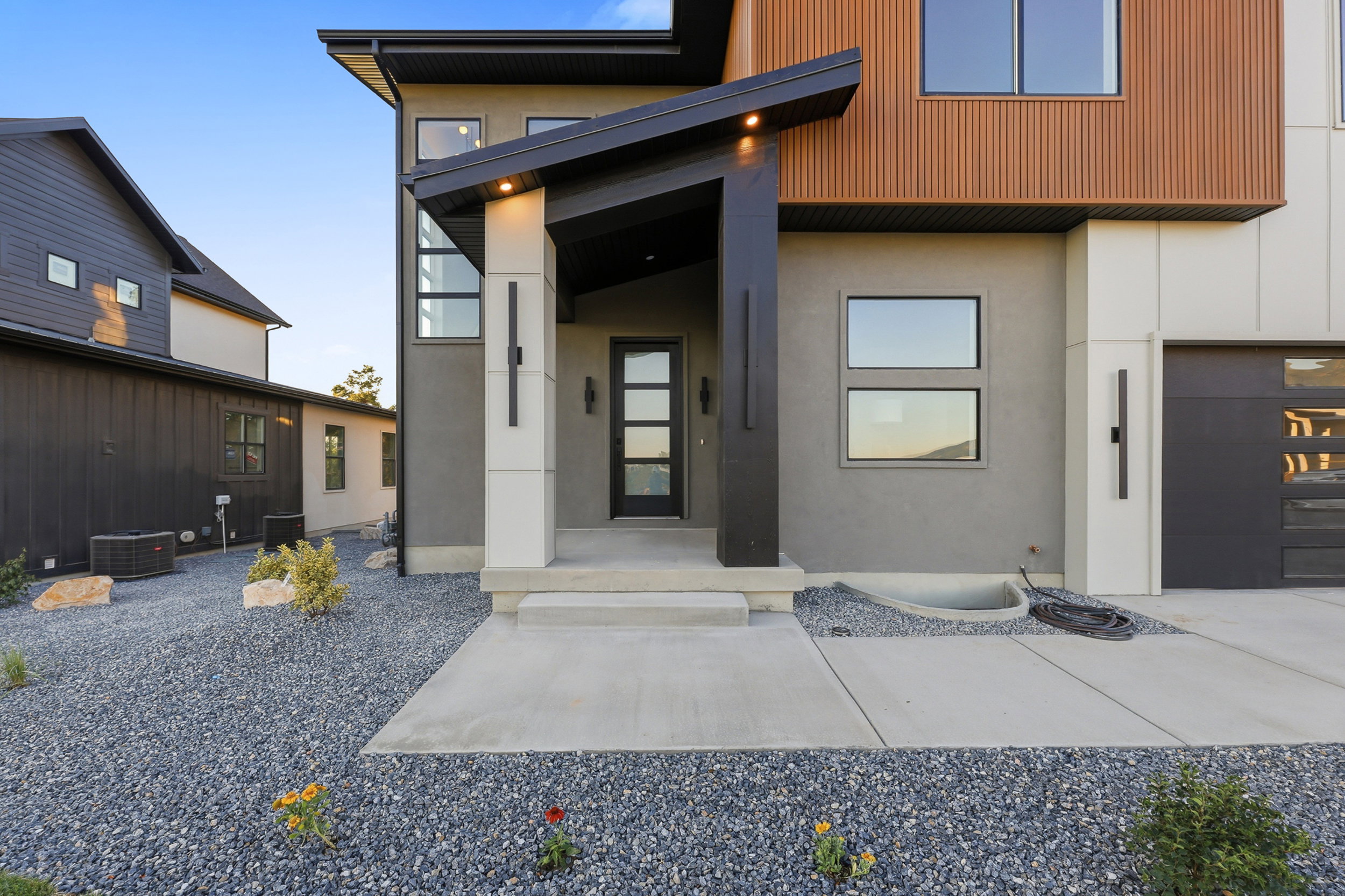 Contemporary exterior featuring contrasting facade materials, an inviting covered entryway, a glass-paneled entry door, a modern garage door, and a gravel landscape