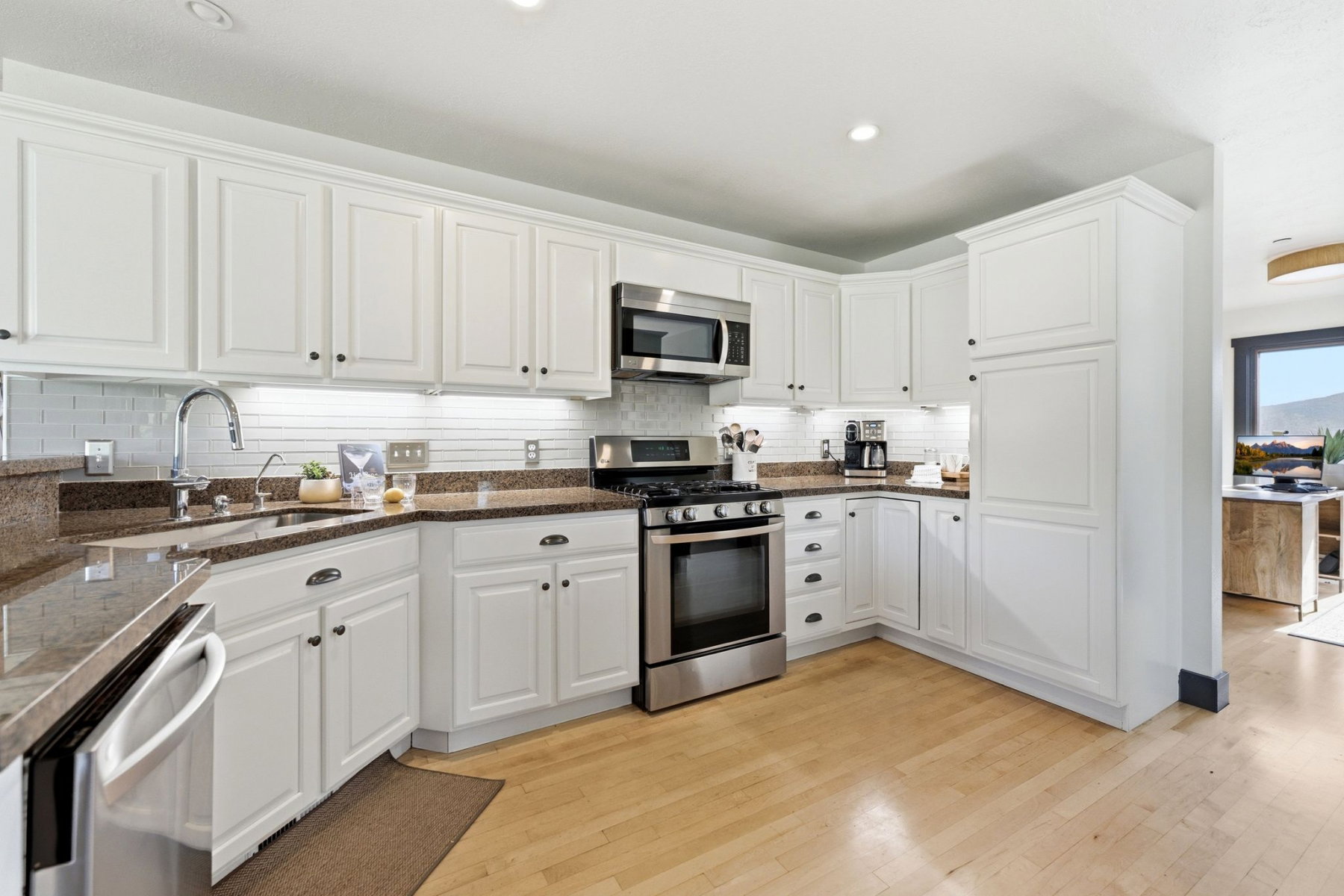 U-shaped kitchen featuring white cabinetry with dark hardware, granite countertops, subway tile backsplash, stainless steel appliances, and wood-finish flooring