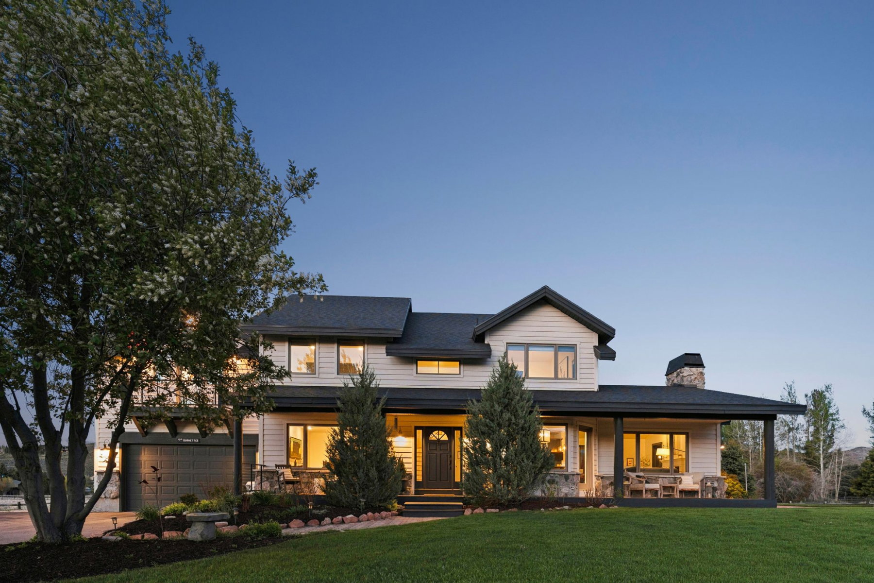 Spacious two-story residence featuring a covered front porch, an attached garage, a prominent stone chimney, a stone façade accent, and a manicured lawn