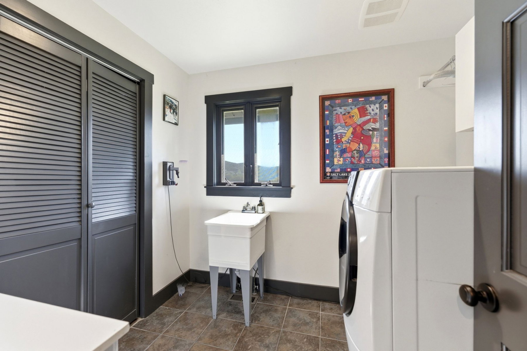 Laundry area featuring louvered bi-fold doors, a utility sink, and tiled flooring