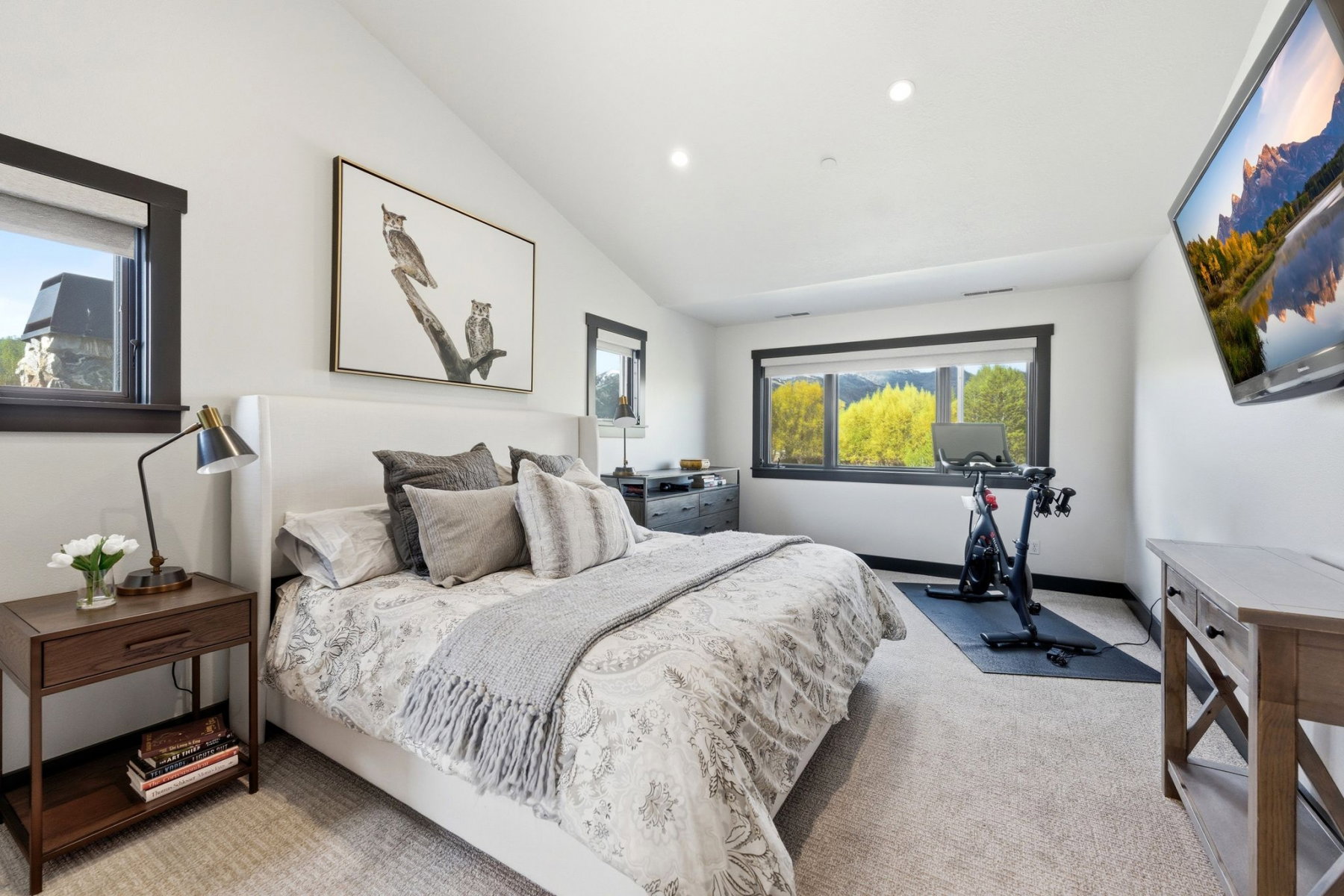 Spacious room featuring vaulted ceilings, recessed lighting, carpet flooring, and multiple windows with dark trim