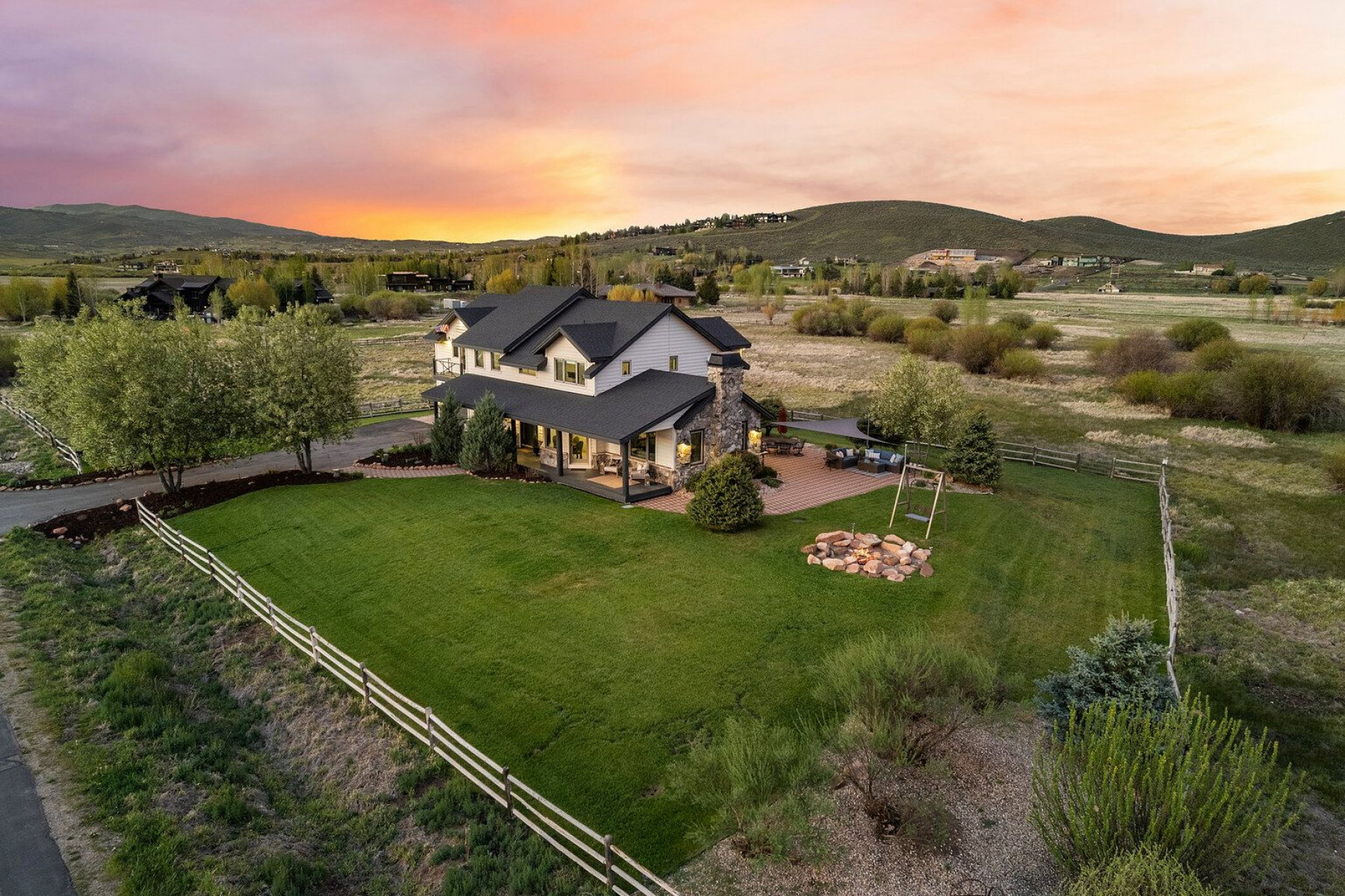 Expansive green lawn featuring a fire pit and patio area, complemented by a large residence with a covered porch and stone chimney