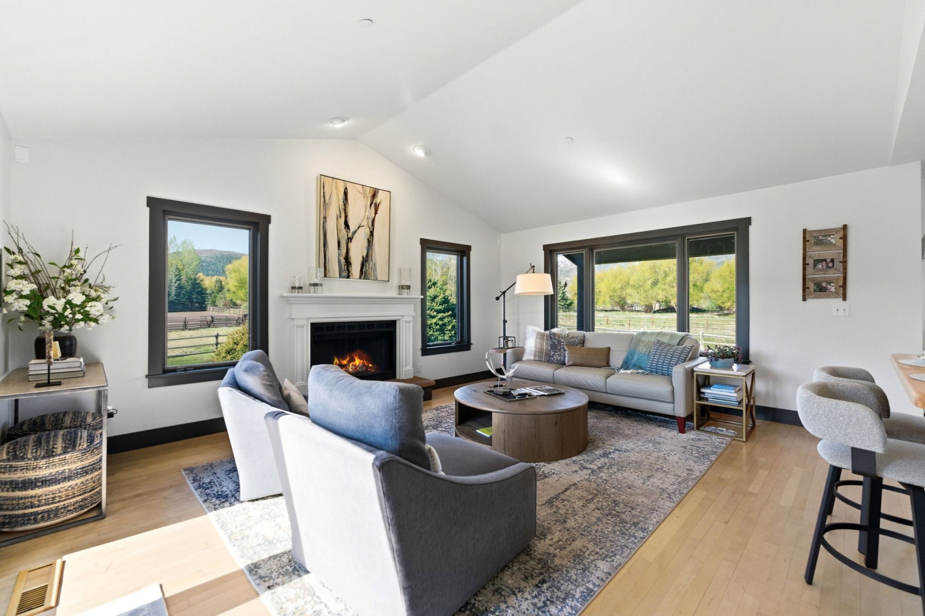 Spacious living area featuring a vaulted ceiling, light wood-finish flooring, and a classic fireplace with white mantel and hearth